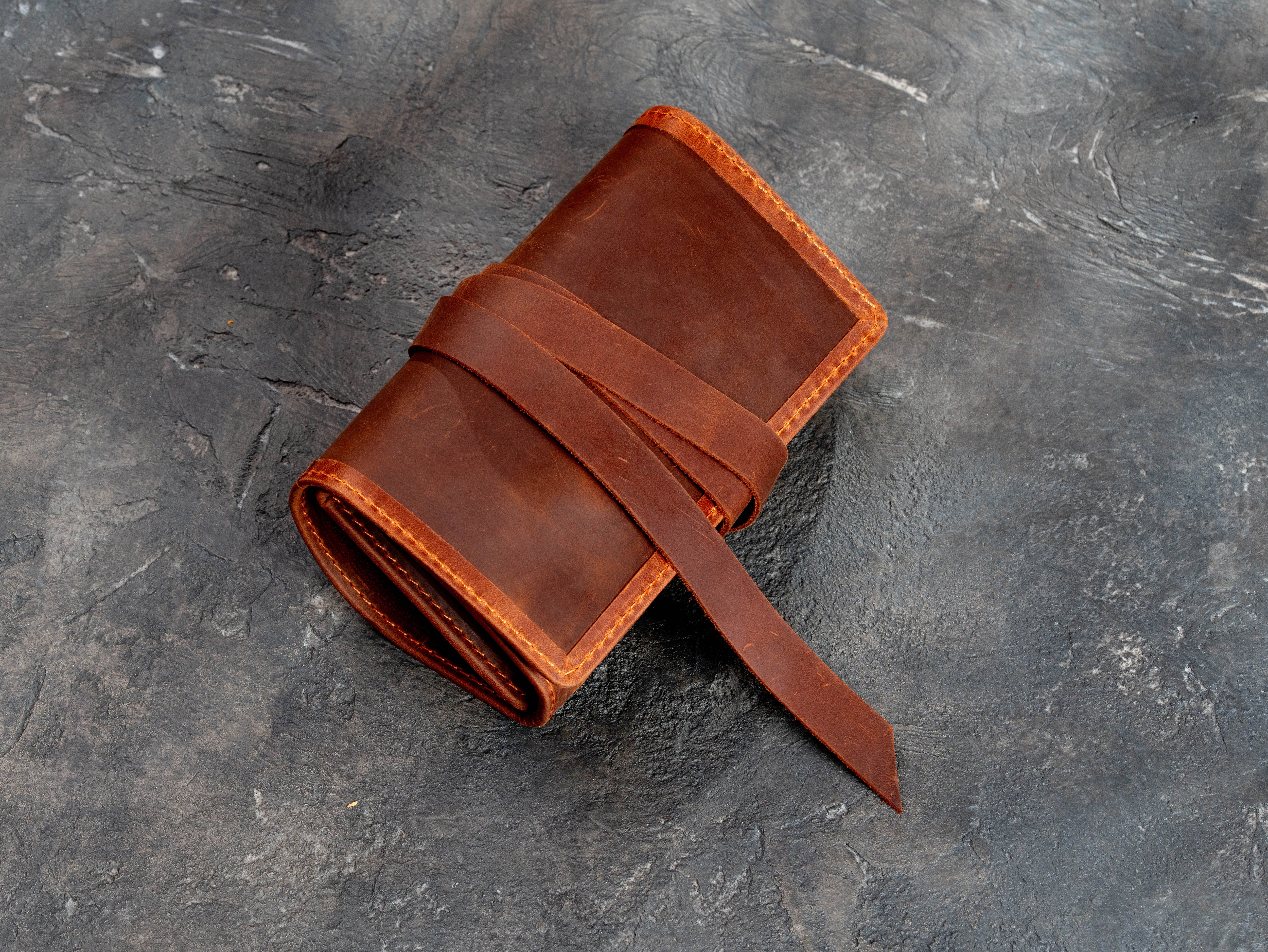 Closed copper leather smoking pipe organizer roll secured with a wraparound leather strap
