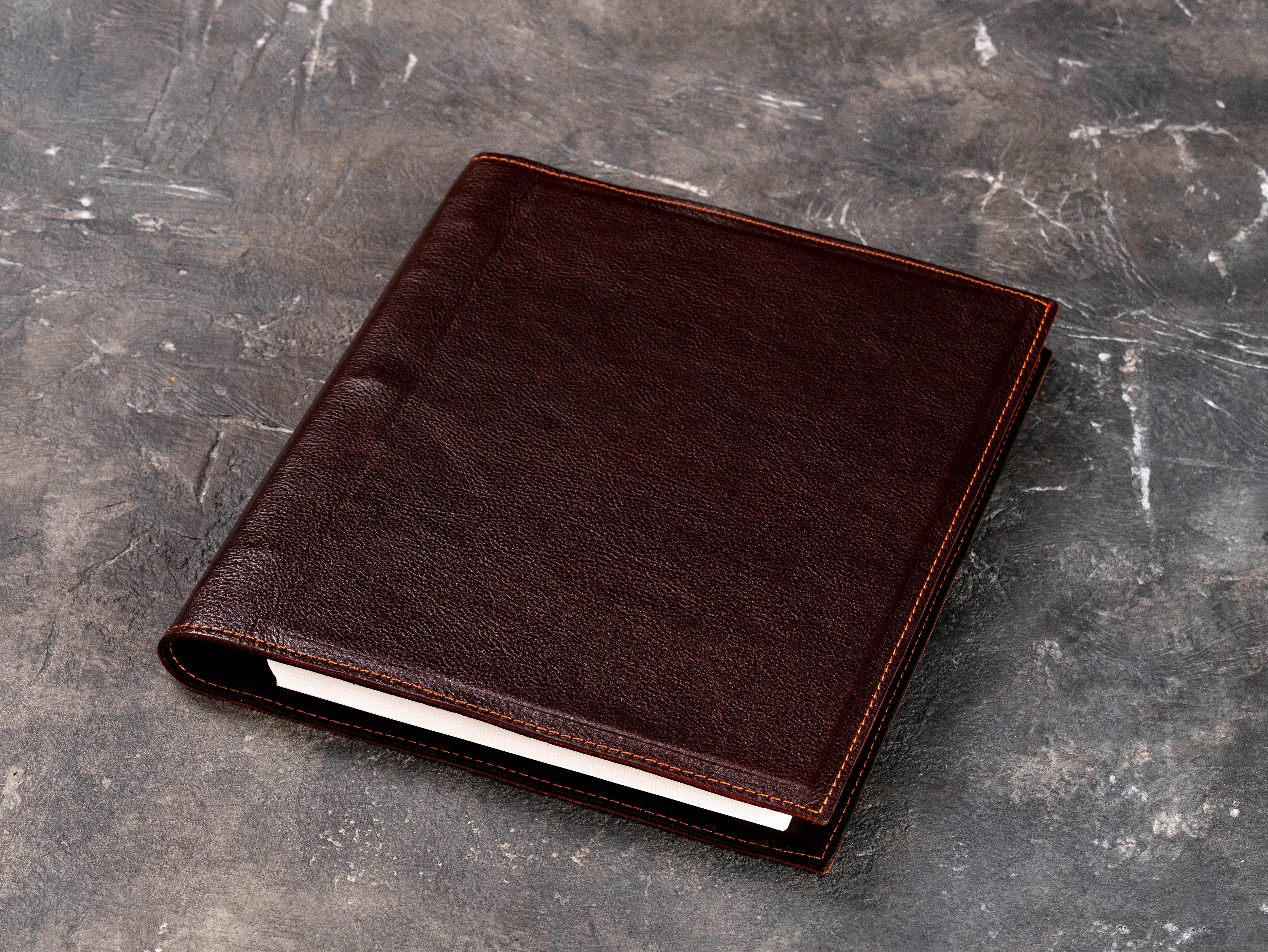Dark brown leather 3-ring binder folder shown at an angle on a textured background