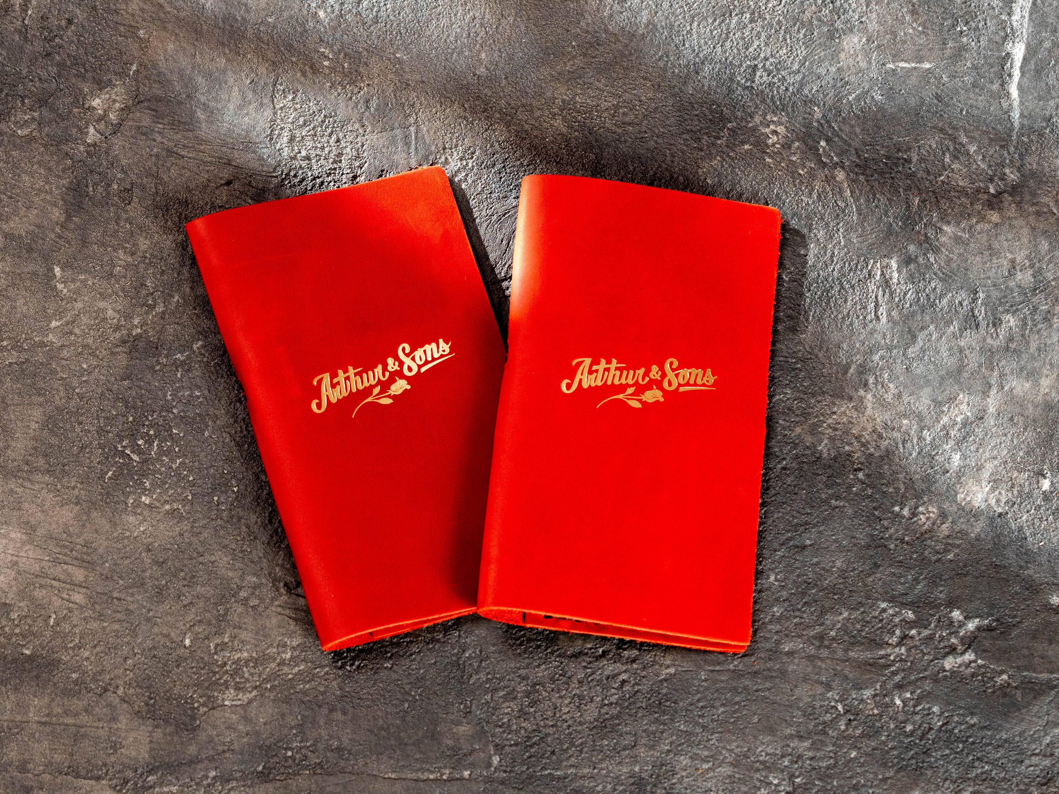 Two red leather restaurant bill holders with gold Arthur & Sons logo on the front