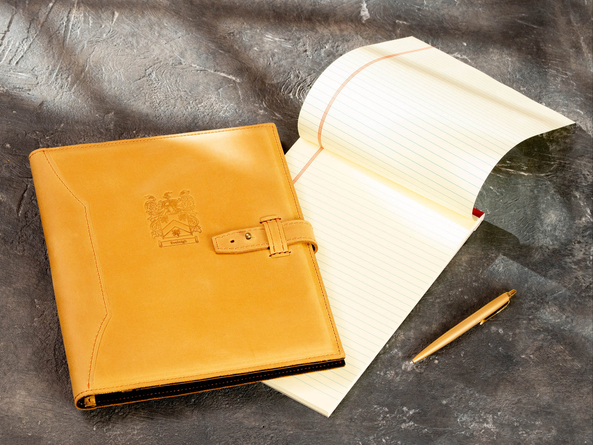 Lifestyle view of personalized wheat leather portfolio with custom crest and closure strap