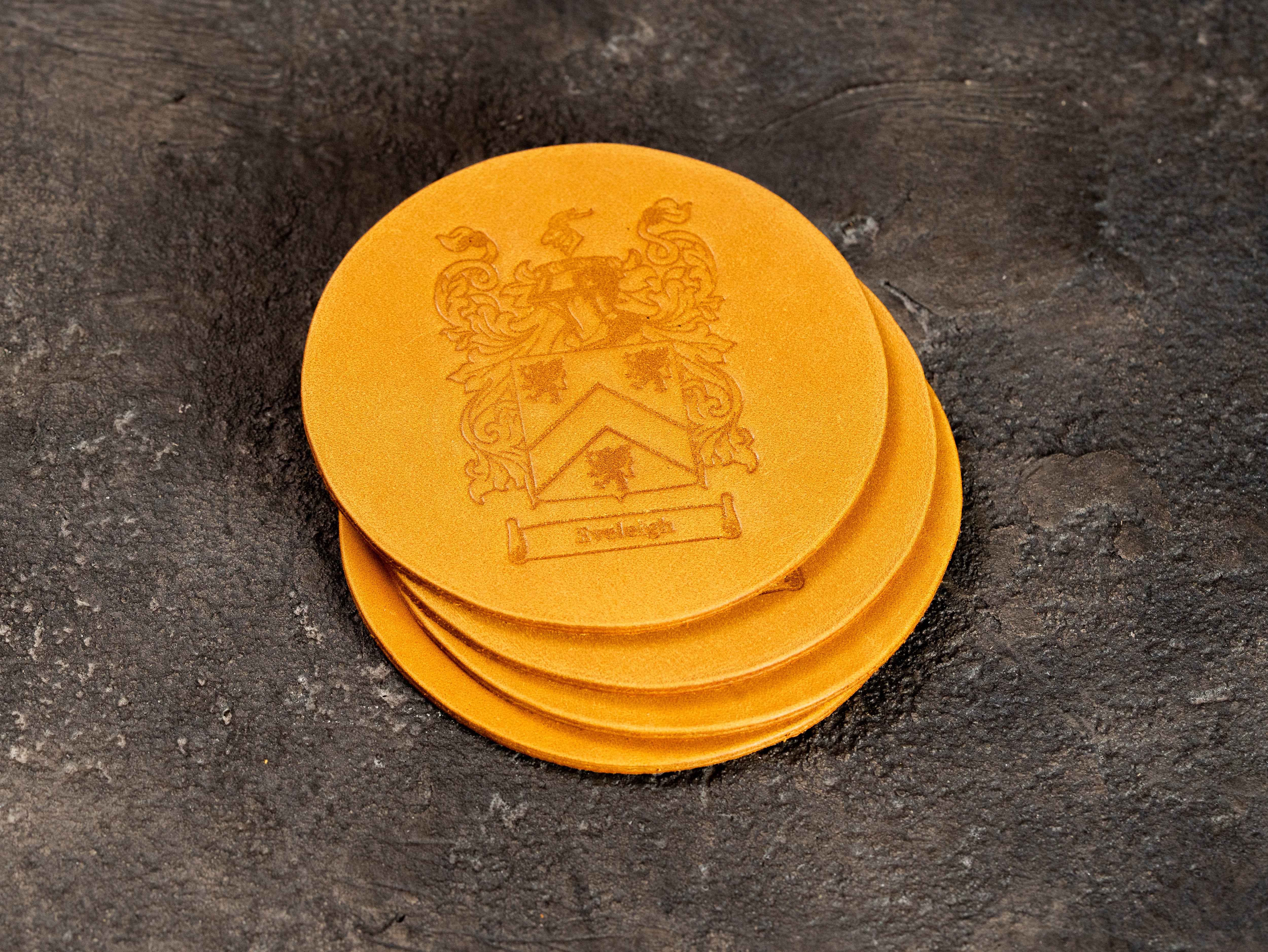 Round yellow leather coasters with custom crest embossing, created as matching accessories for a personalized leather portfolio.