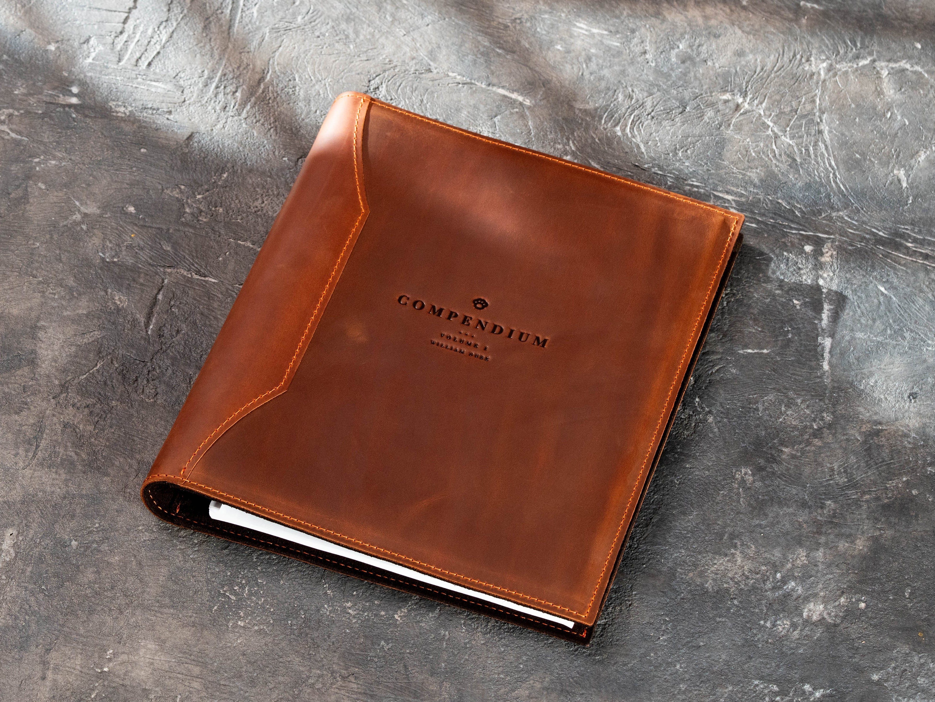 Brown leather business document binder with Compendium logo and stitched cover.