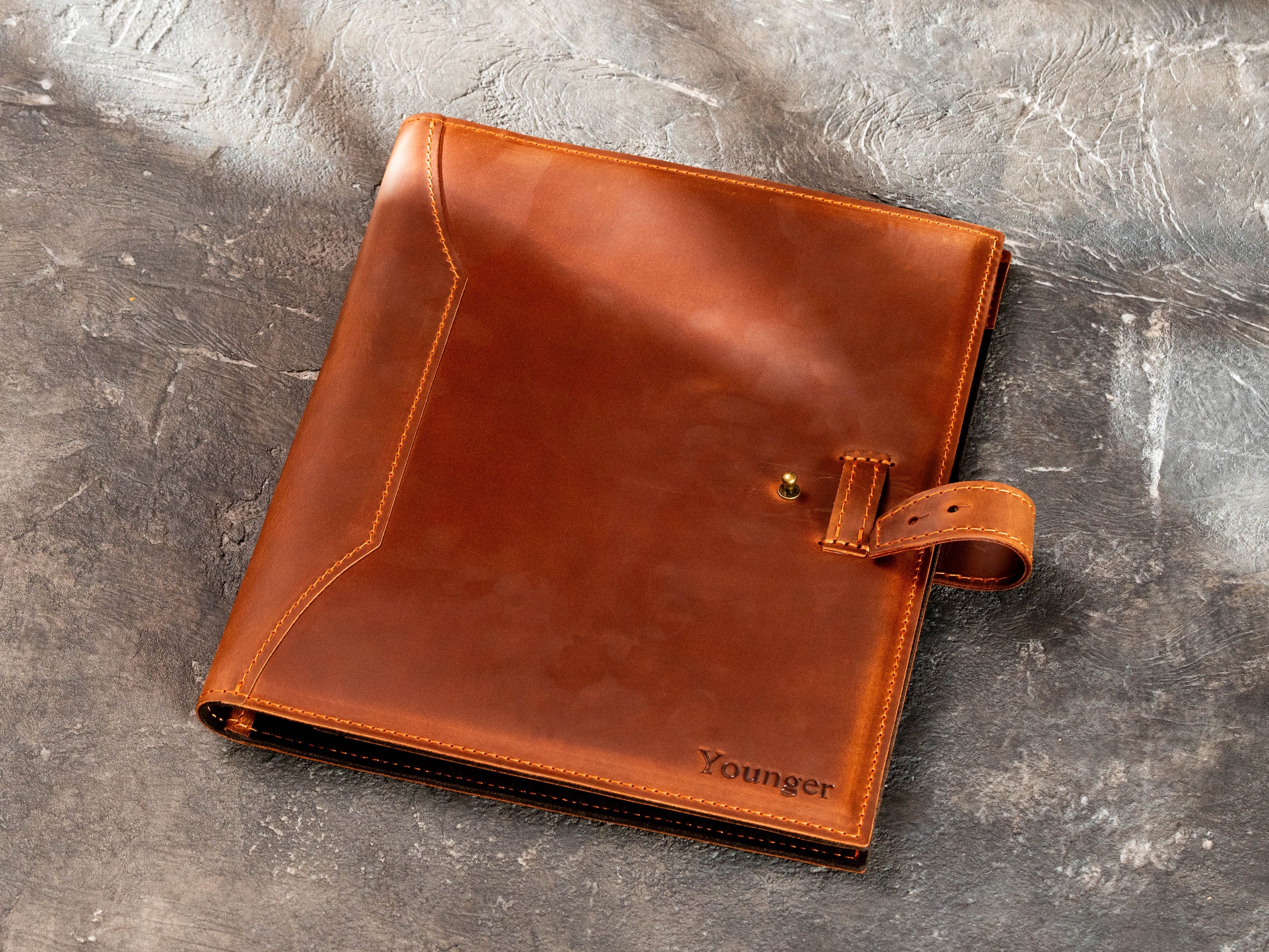 Copper leather portfolio with strap closure open to show fastening detail.