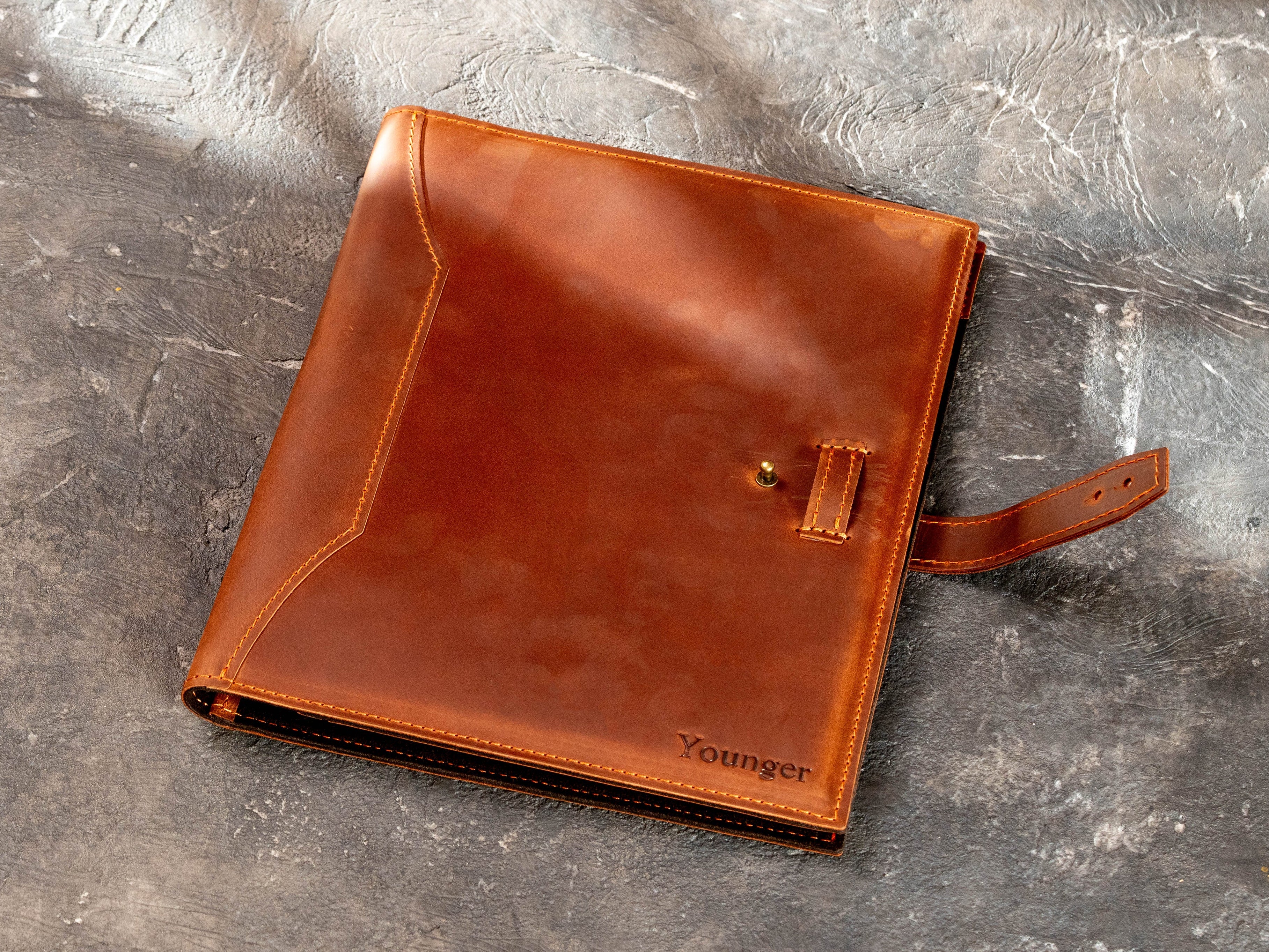 Personalized leather business portfolio with adjustable leather strap and metal stud closure.