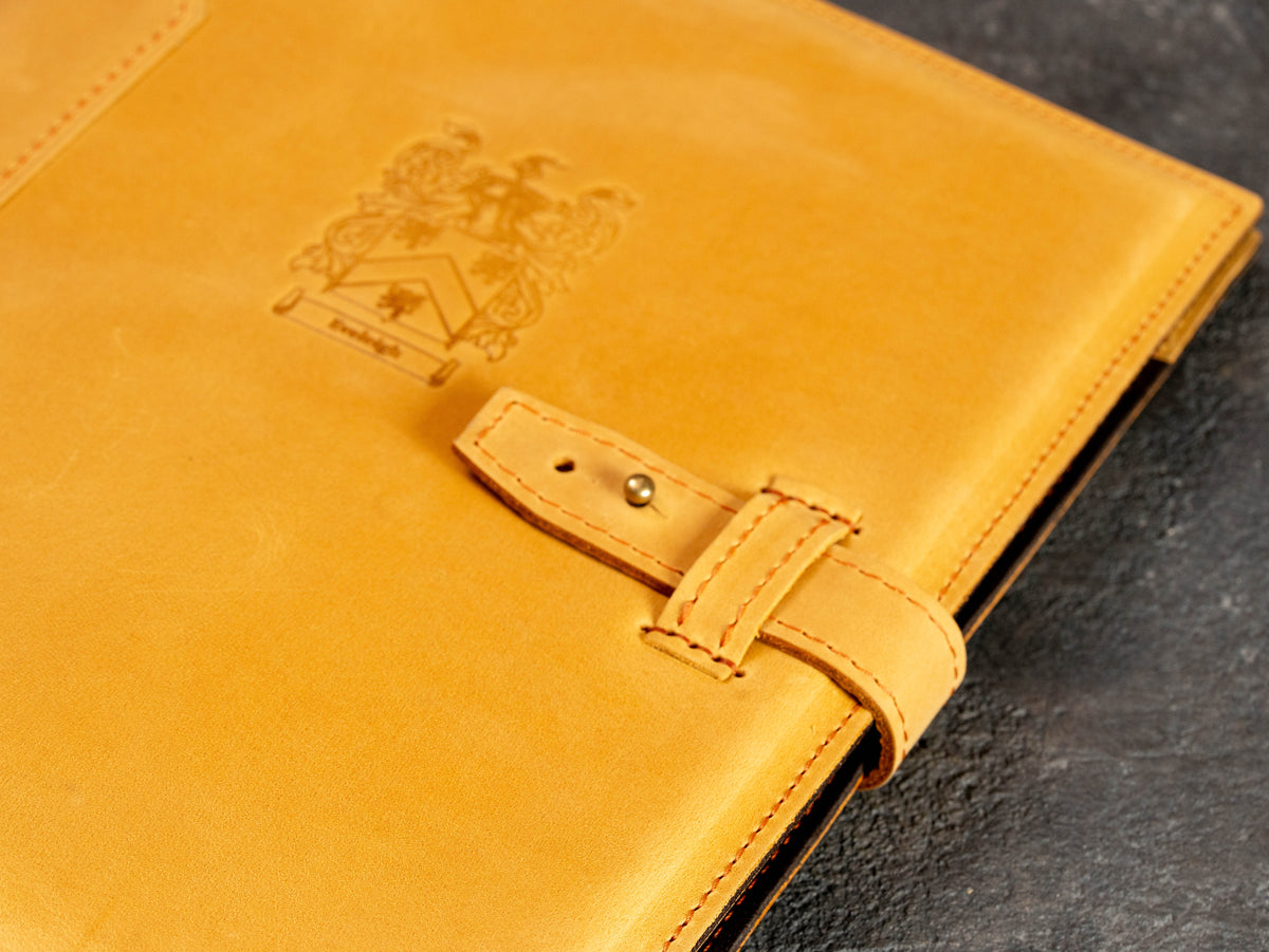 Close-up of custom crest personalization and leather strap closure on wheat portfolio