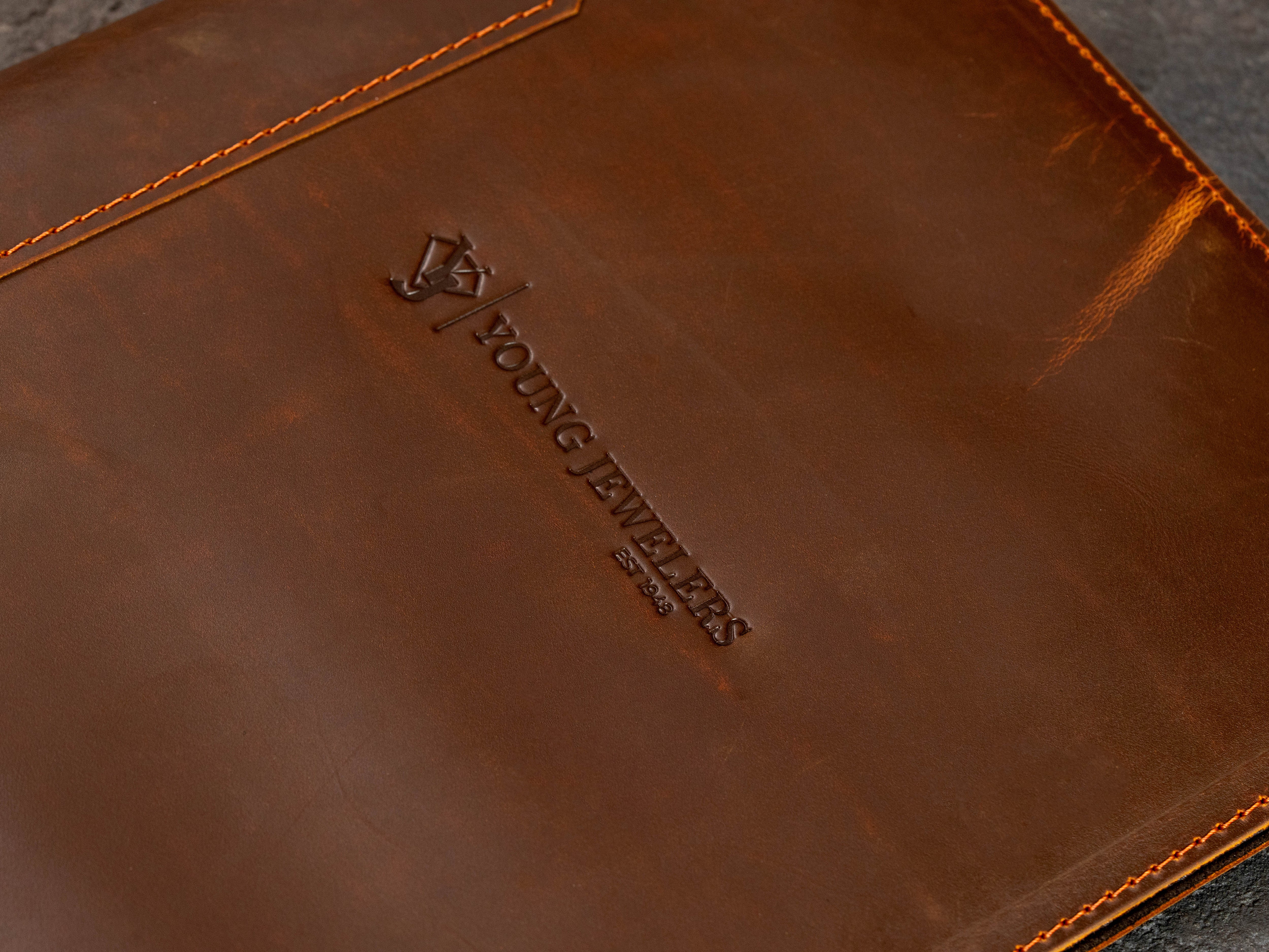 Close-up of embossed company logo on brown leather presentation binder with natural leather texture.