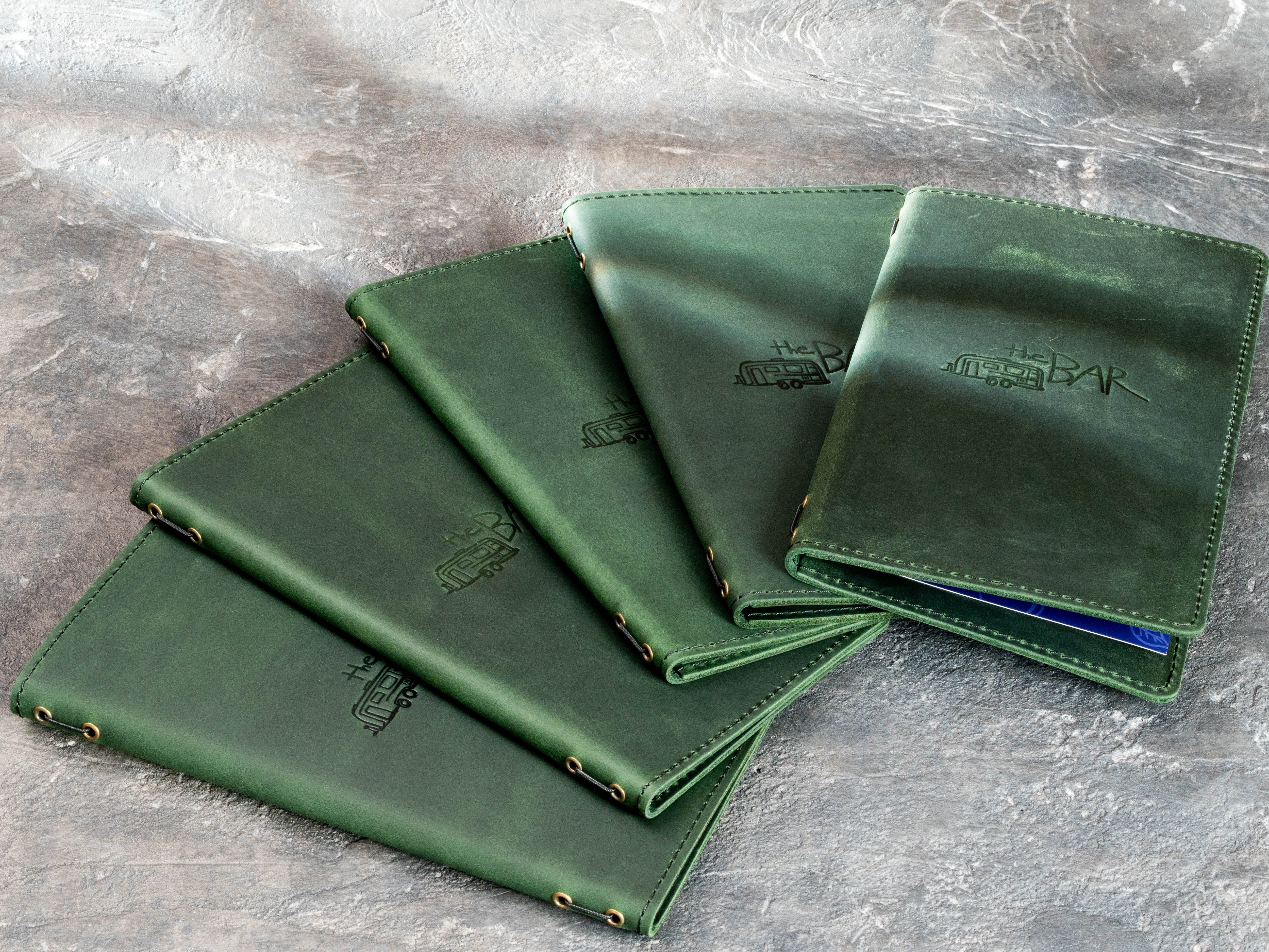 Custom green leather bar menu covers made as a coordinated batch for a hospitality client.