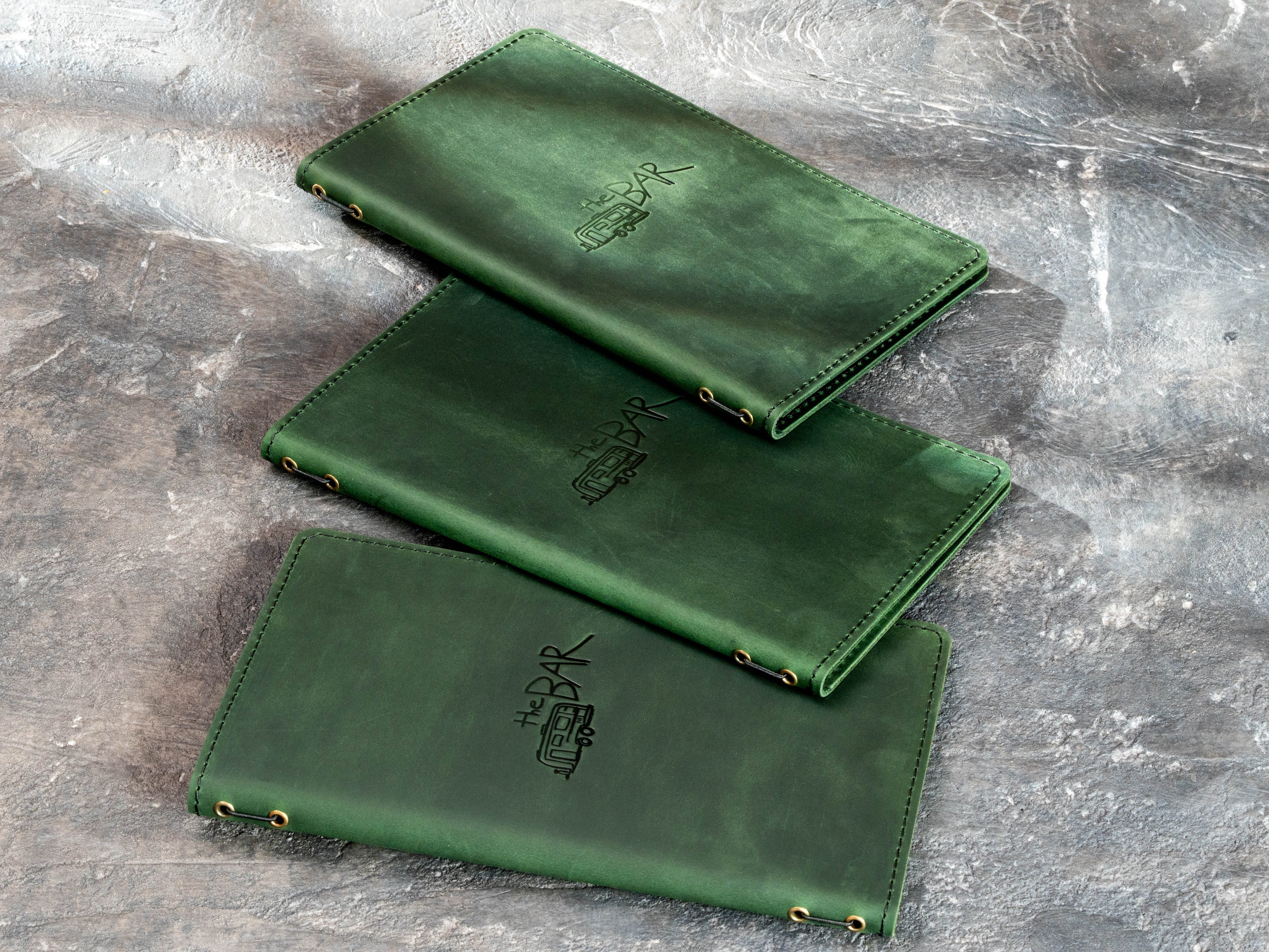 Custom green leather bar menu covers with logo embossing, elastic cord binding, and double-layer construction.