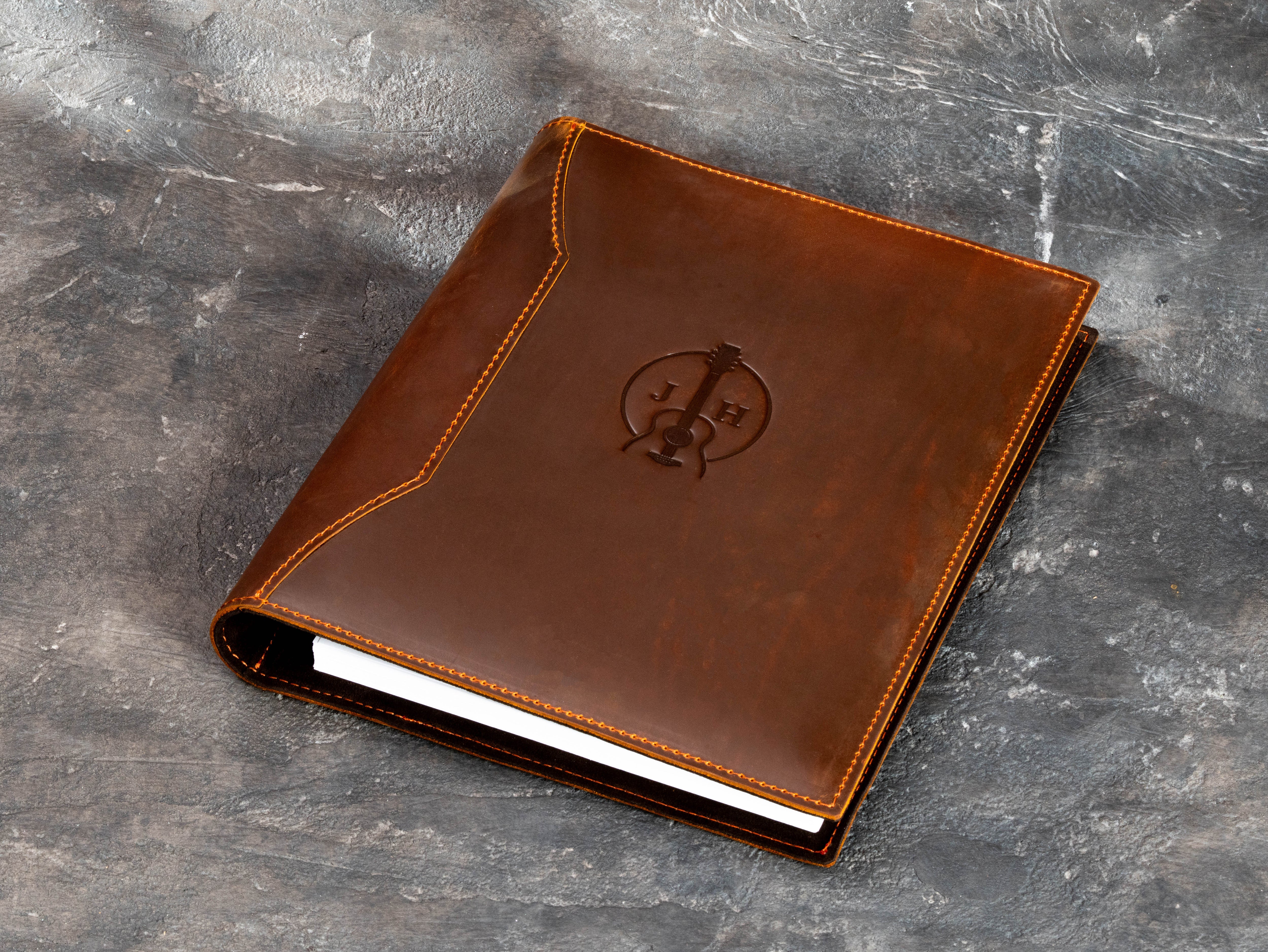 Warm brown leather musician binder with custom embossed guitar emblem and initials, designed for A4 and 8.5 × 11 inch pages.