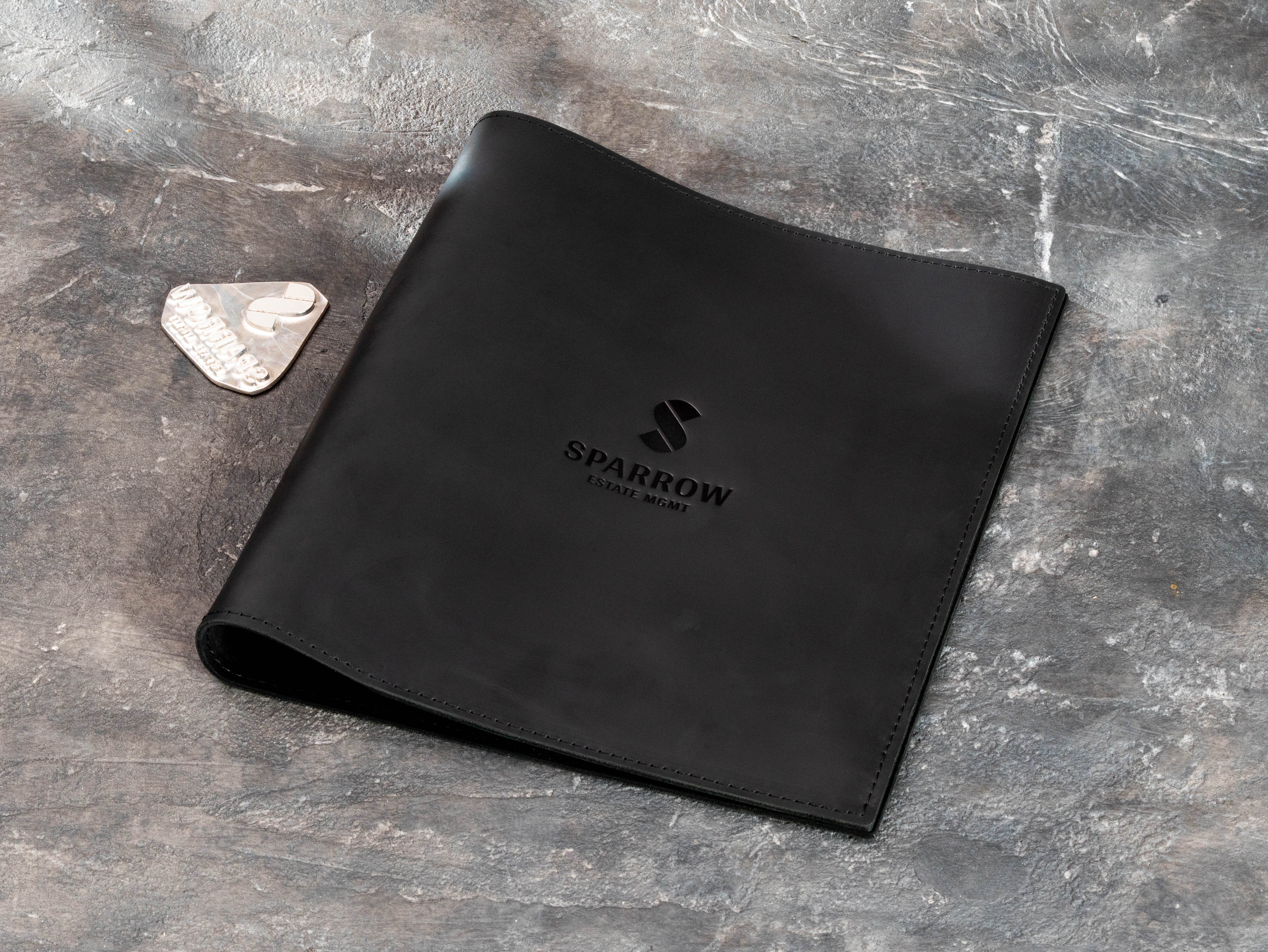 Black leather portfolio folder with client logo and branding stamp shown beside the binder
