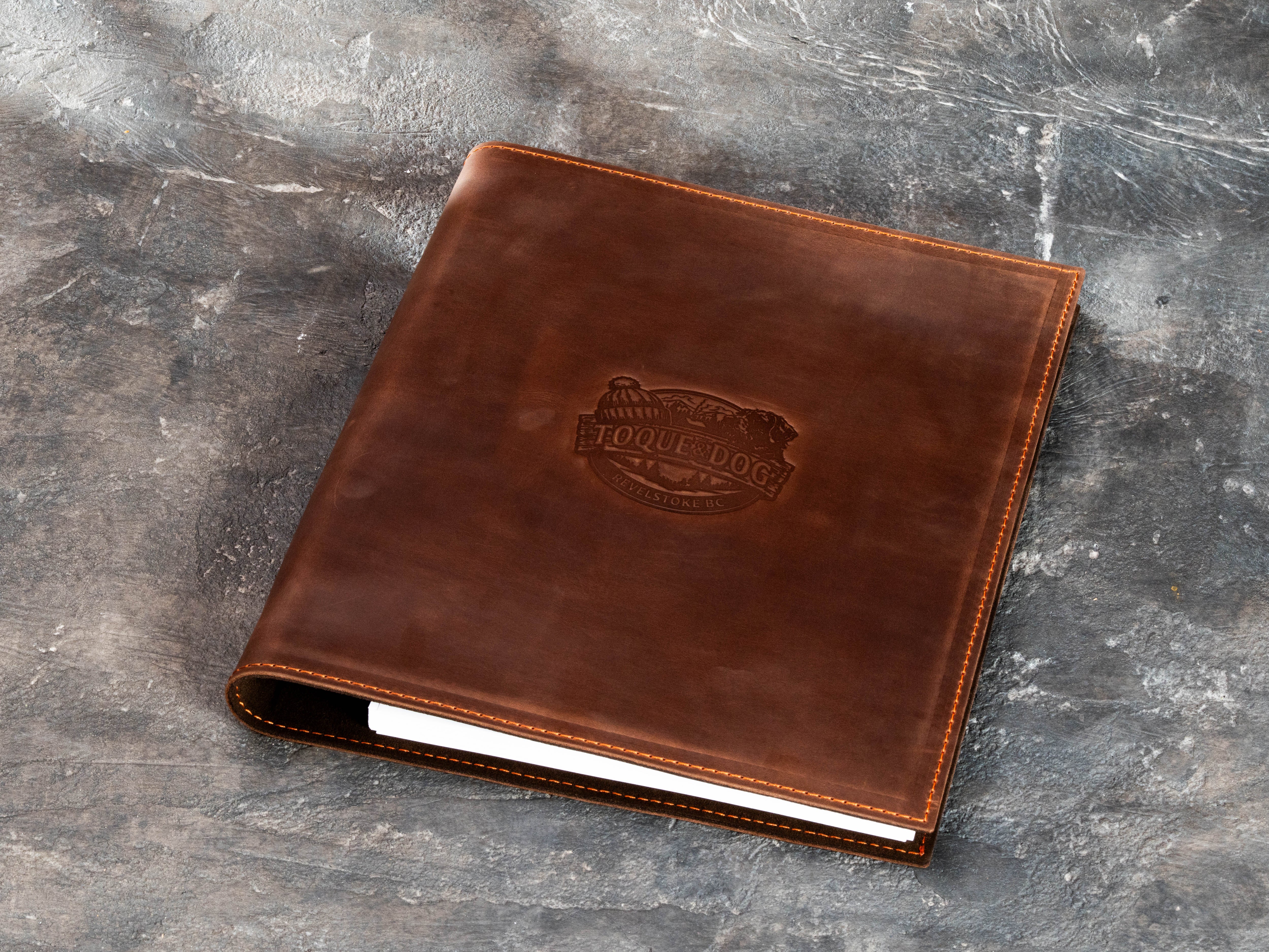 Personalized warm brown leather travel folder with custom logo embossing for a guest information project.