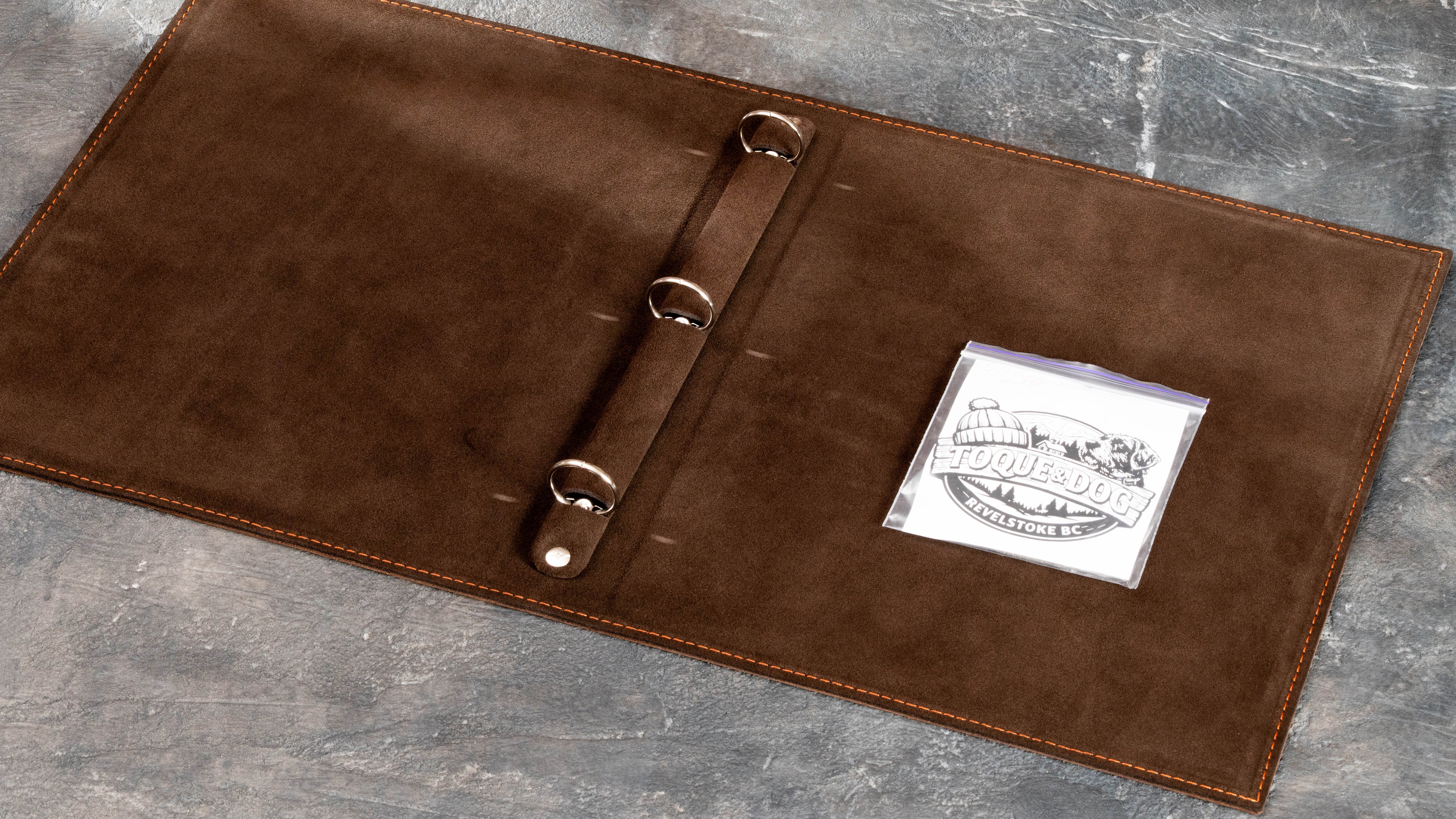 Light suede interior of brown leather guest information binder with 3-ring mechanism and custom logo artwork.