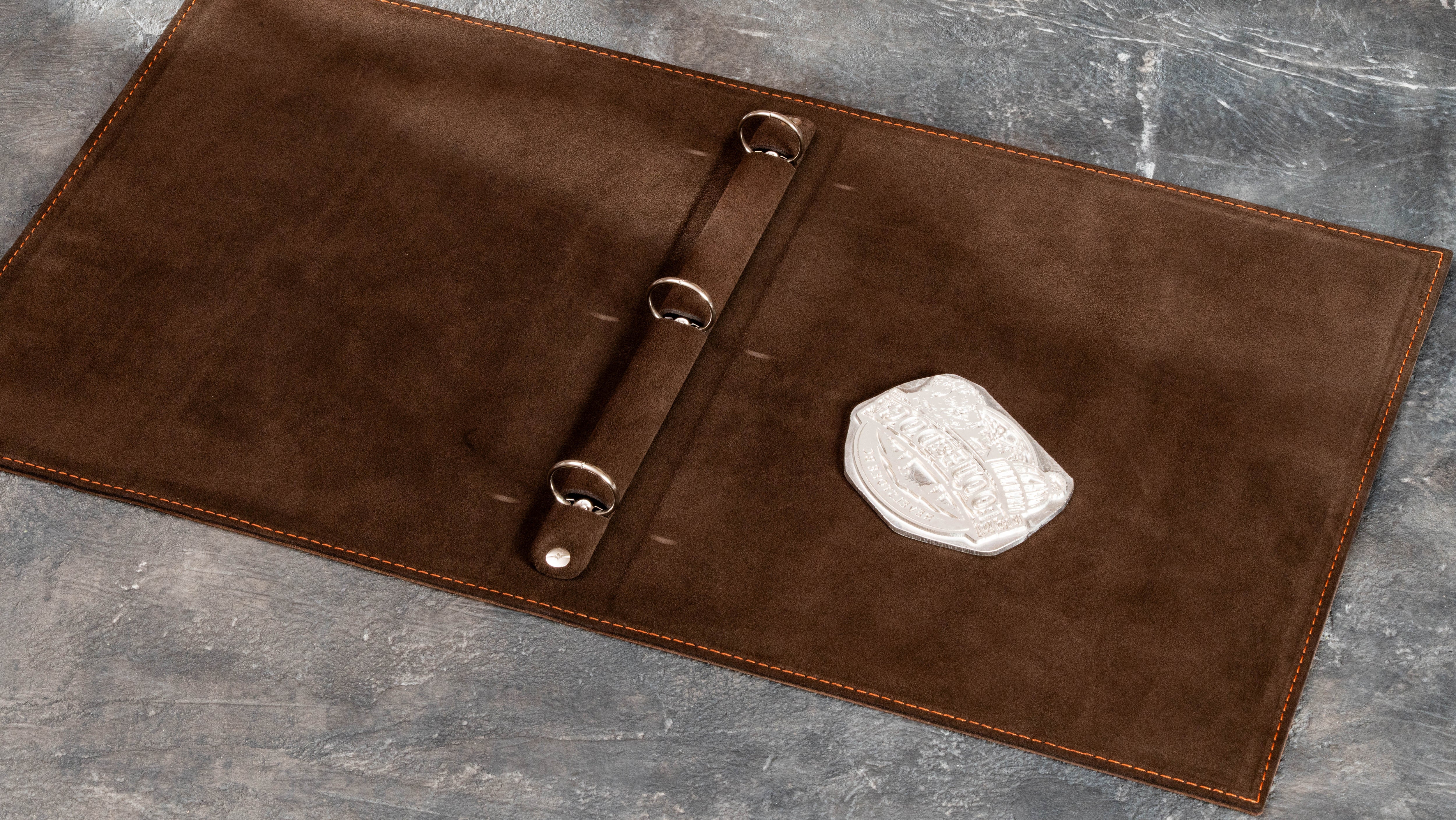 Brown leather travel binder interior with three-ring mechanism and client logo design prepared for embossing.