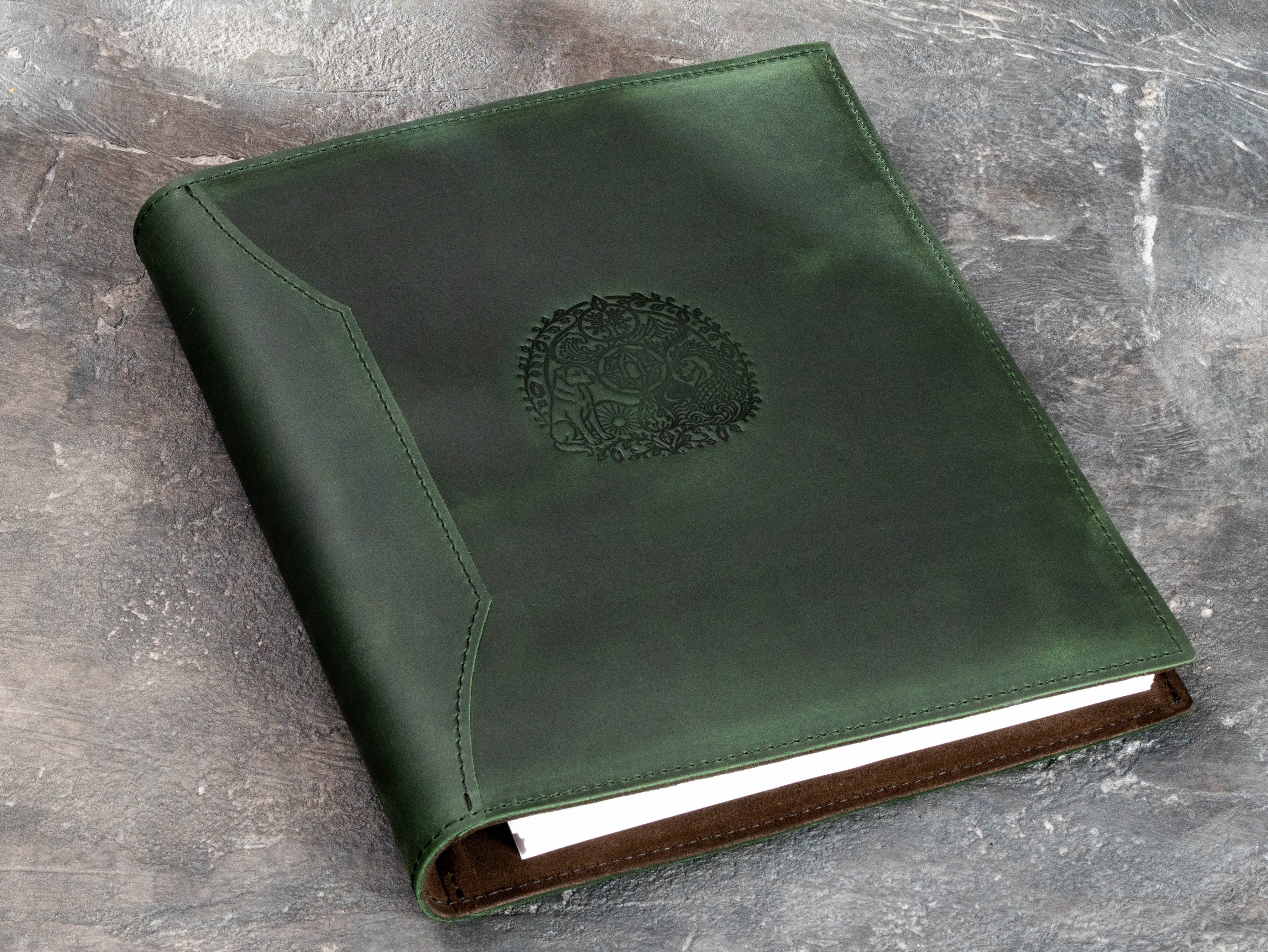 Green leather story binder with decorative embossed design and visible page storage inside