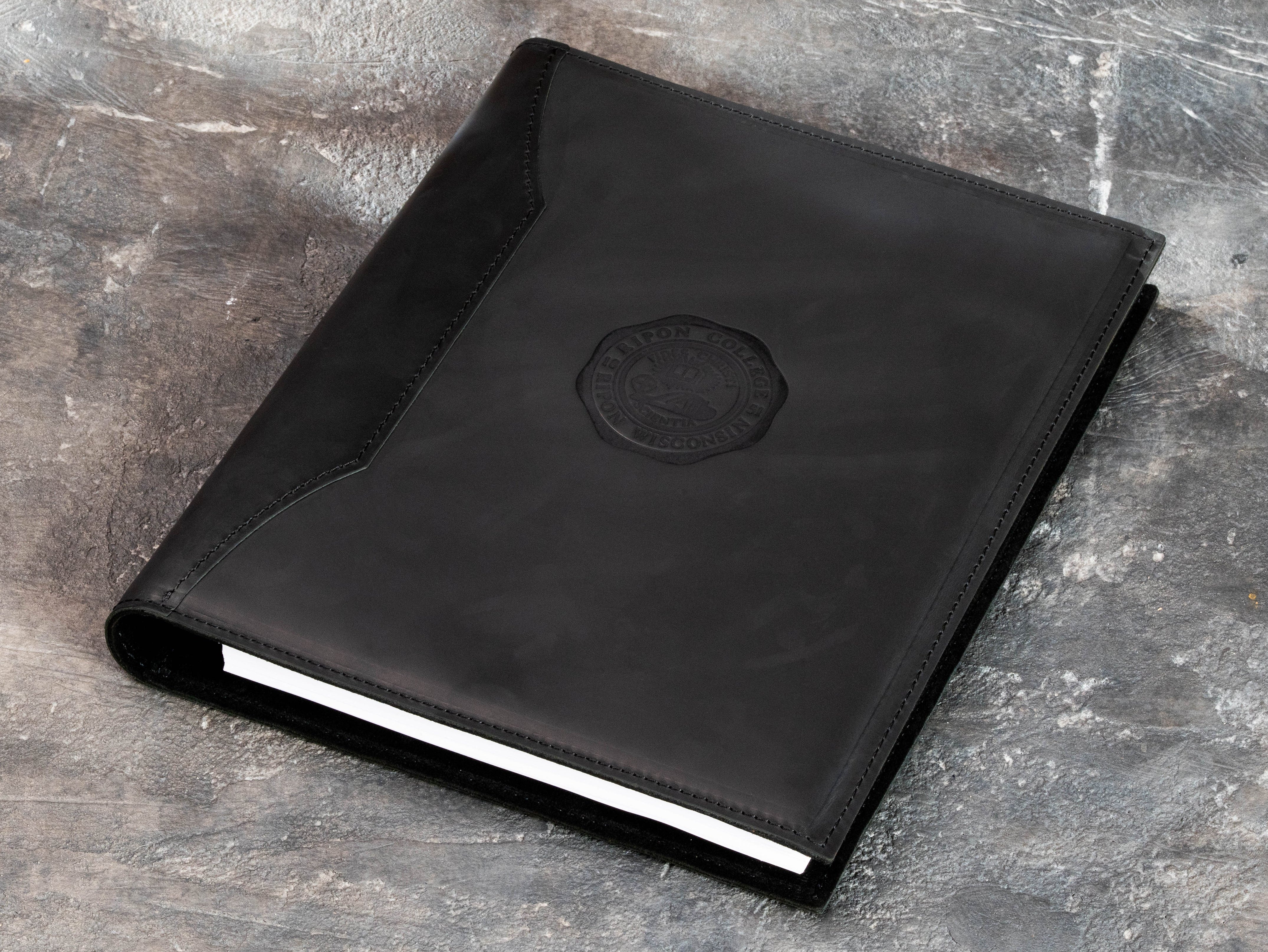 Custom college emblem embossed on black leather with the matching metal embossing die used for personalization.