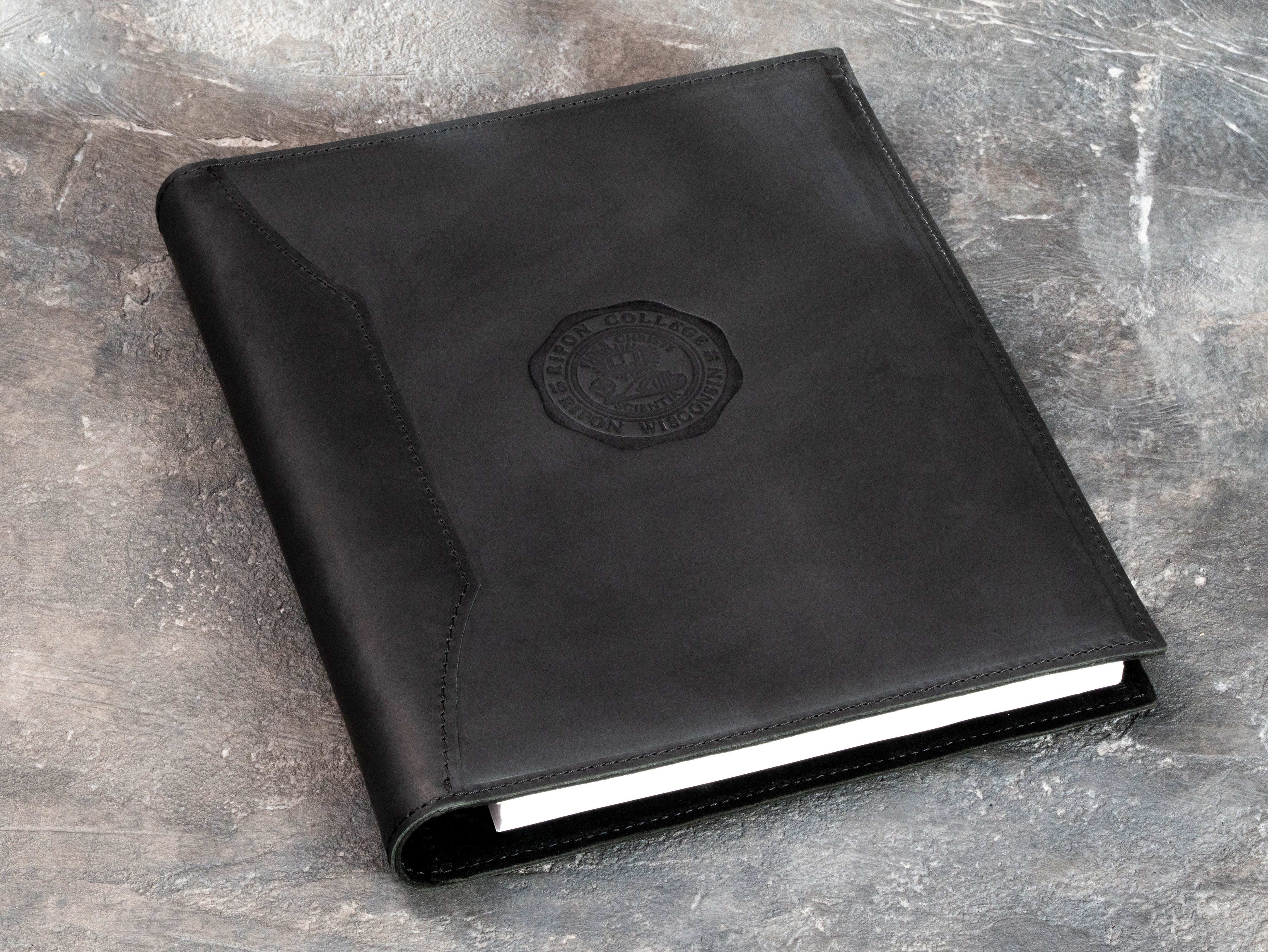 Black leather 3-ring college memory binder with interior suede finish, paper storage and custom embossing die for school emblem personalization.