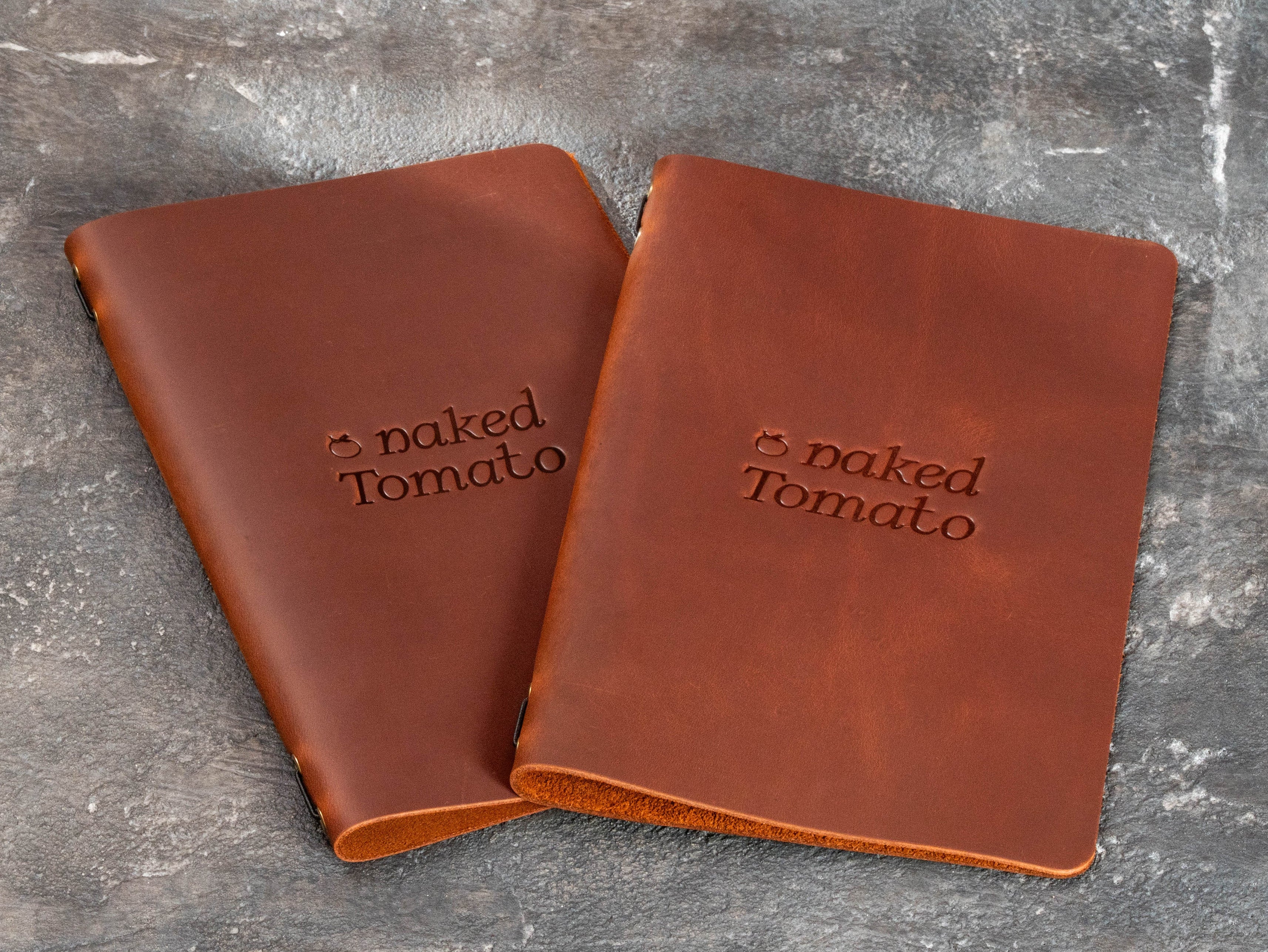 Two brown leather restaurant menu covers with blind embossed Naked Tomato logo and rounded corners