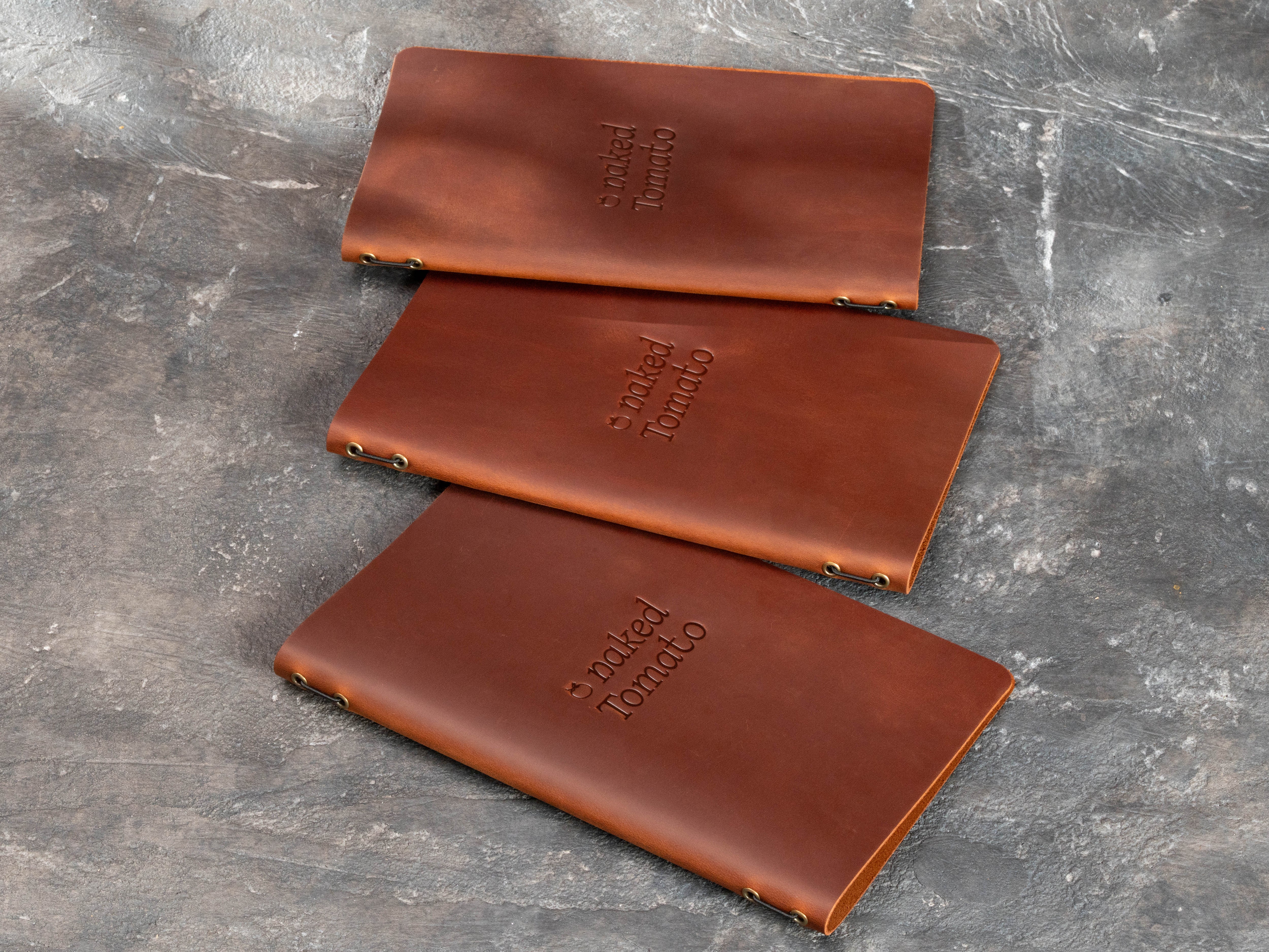 Three brown leather menu books shown from the back with elastic cord binding and metal eyelets