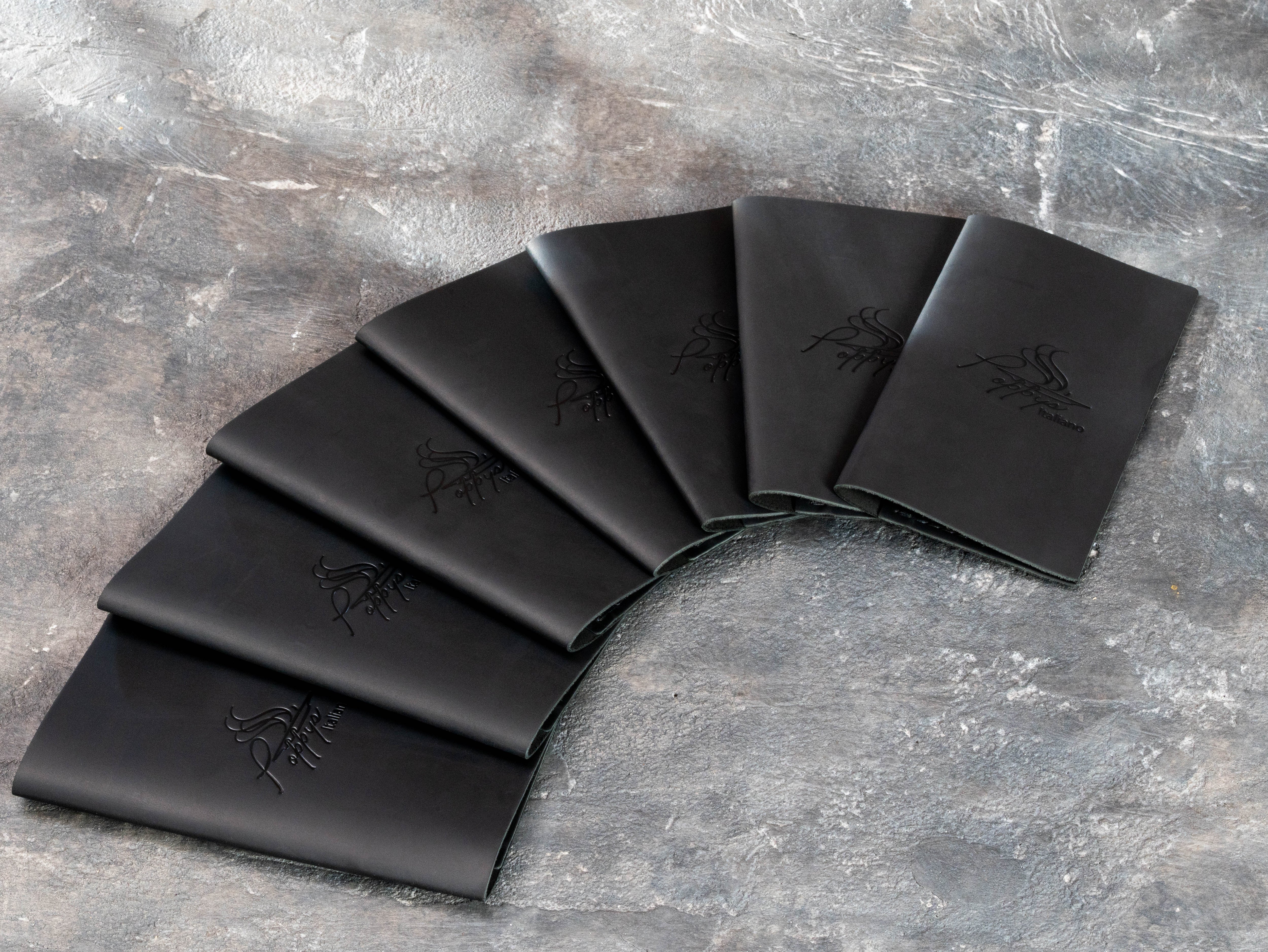 Set of minimalist black leather guest check folders with tone-on-tone blind embossed restaurant logos.