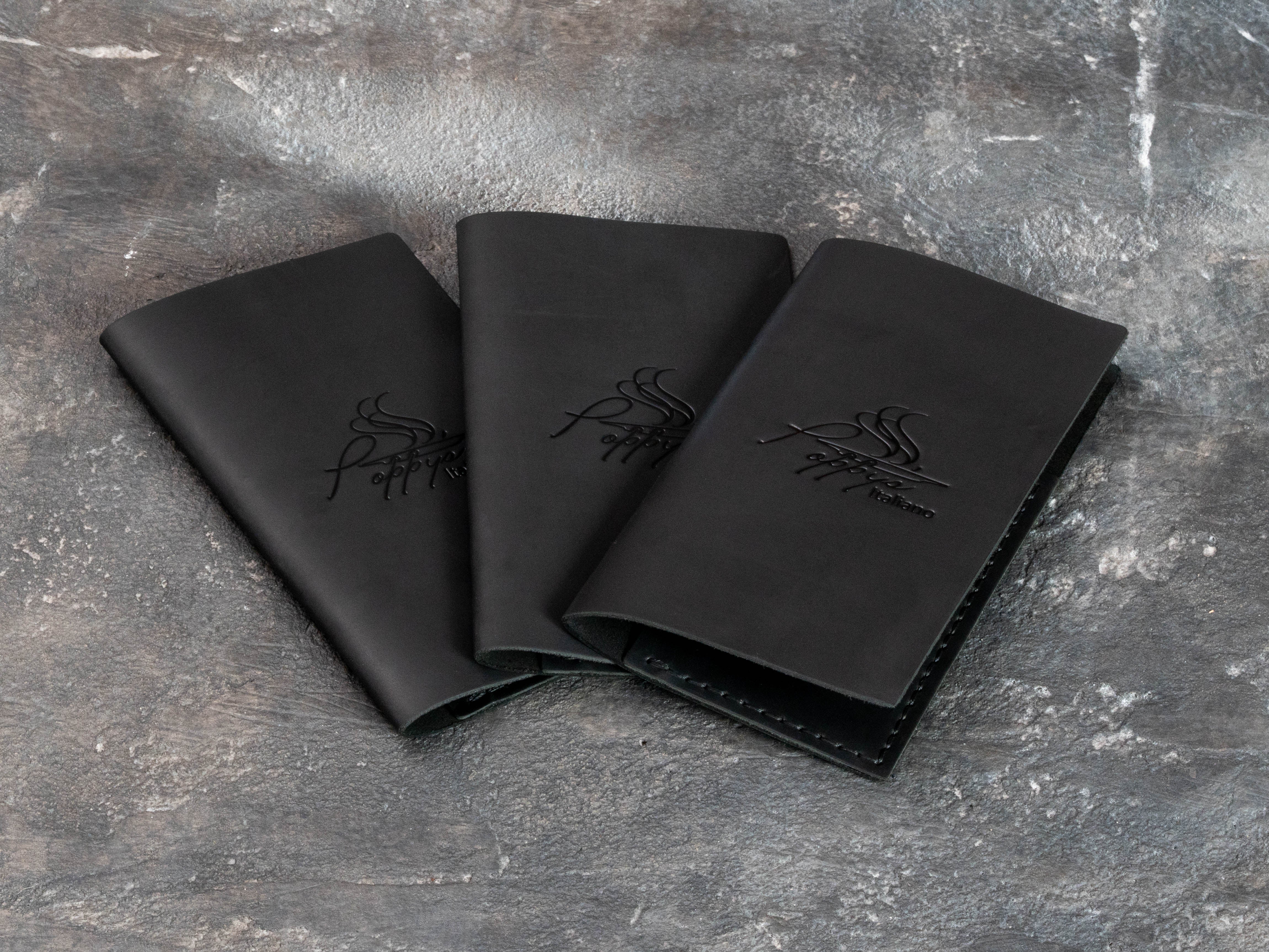 Three black leather restaurant bill holders with subtle black-on-black custom logo embossing.