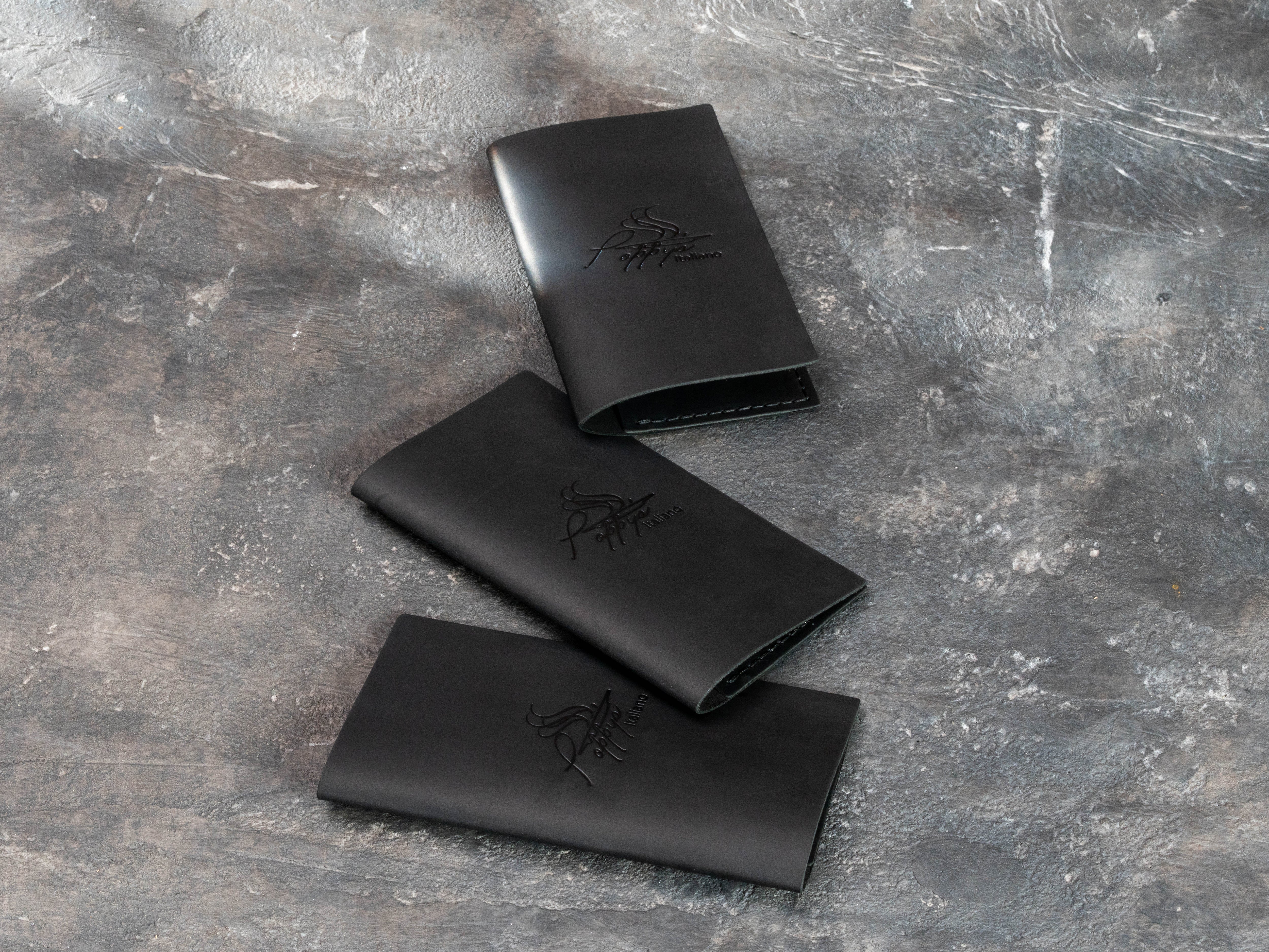 Three minimalist black leather payment folders with blind embossed restaurant logos and compact slim construction.