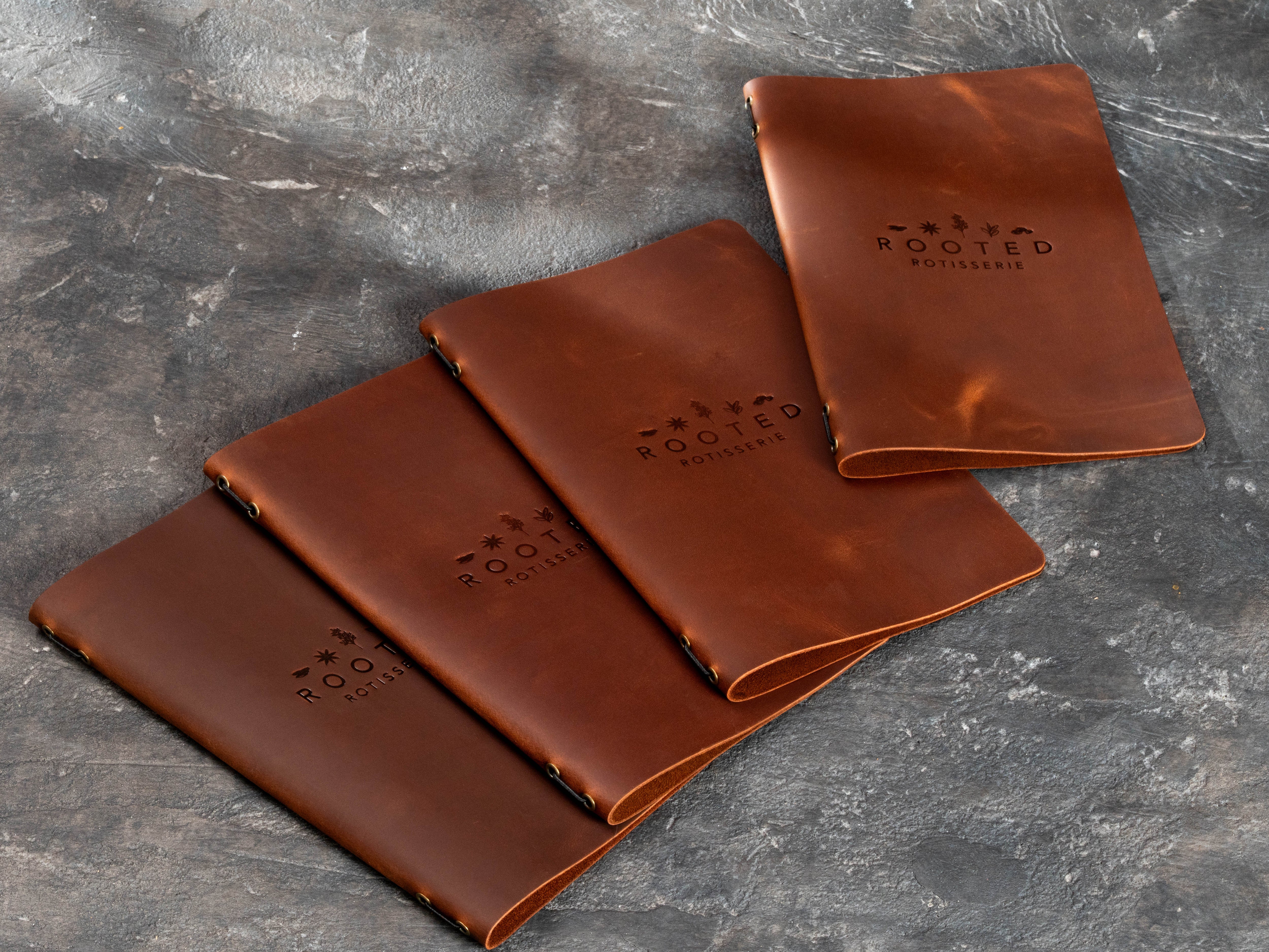Warm brown leather restaurant menu covers made for Rooted Rotisserie with blind embossed logo in several coordinated sizes.