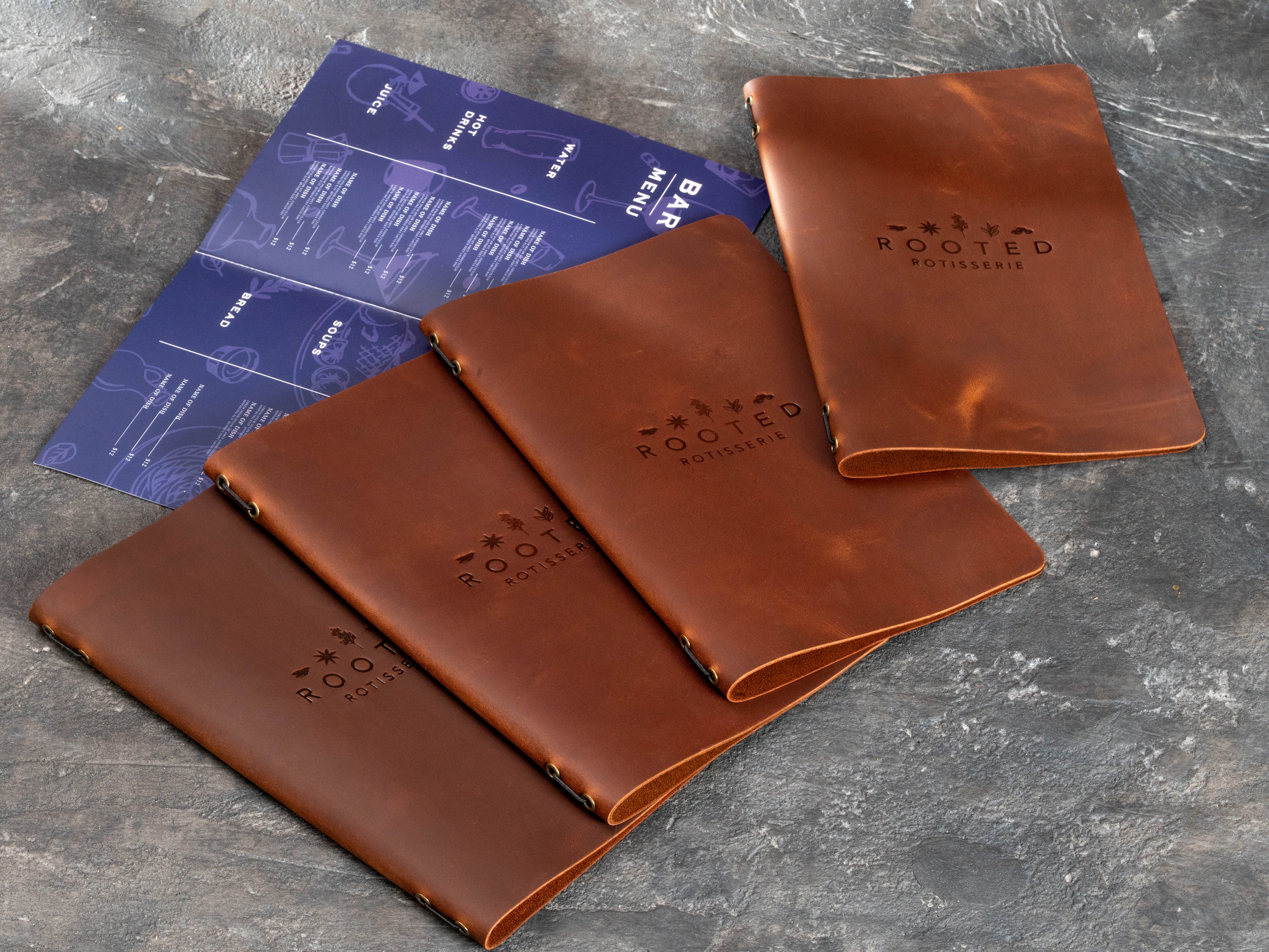 Custom leather menu cover set with Rooted Rotisserie branding and replaceable printed food and bar menu pages.