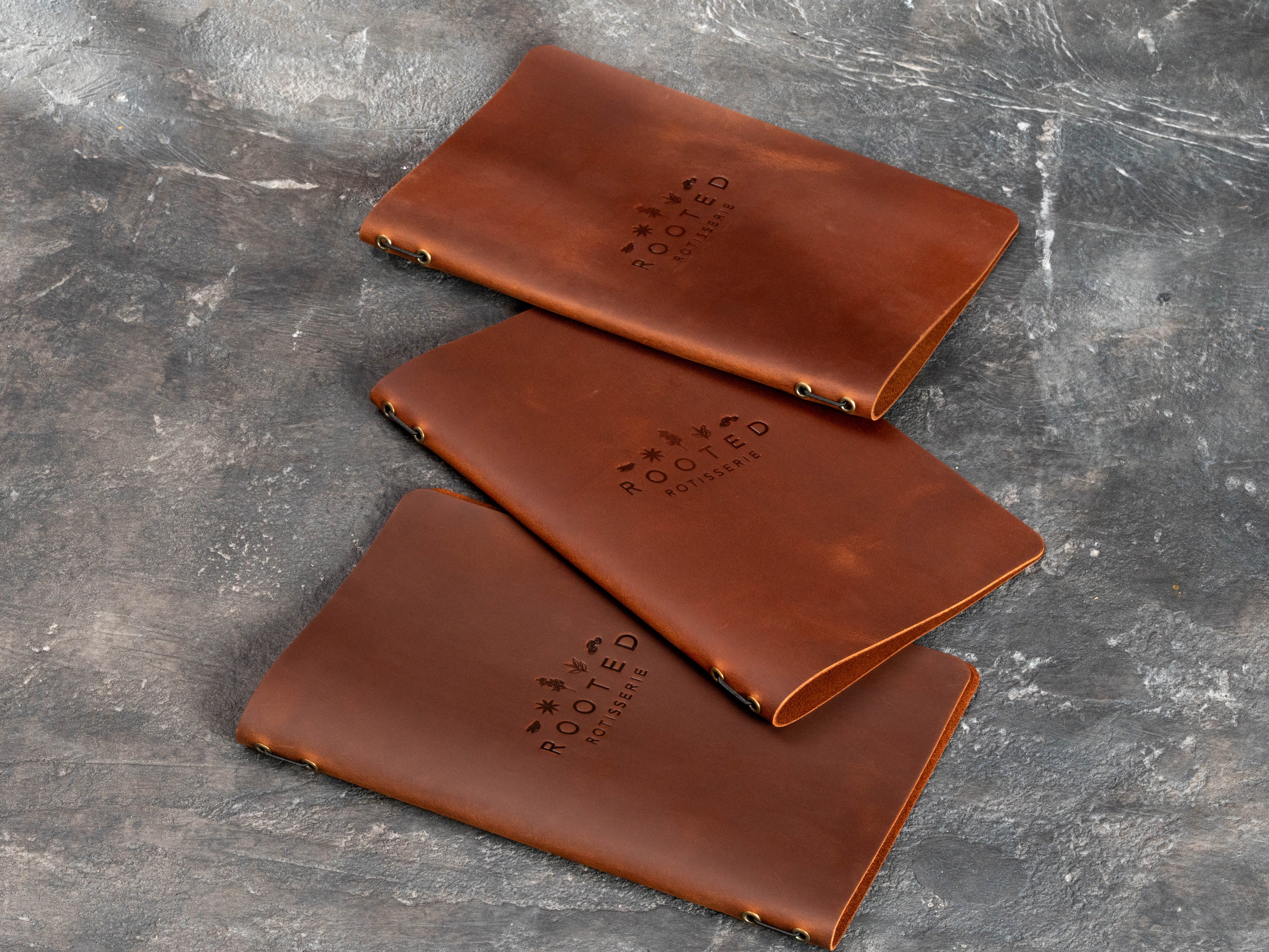 Three custom leather menu covers showing flexible construction, metal eyelets and elastic cord binding.