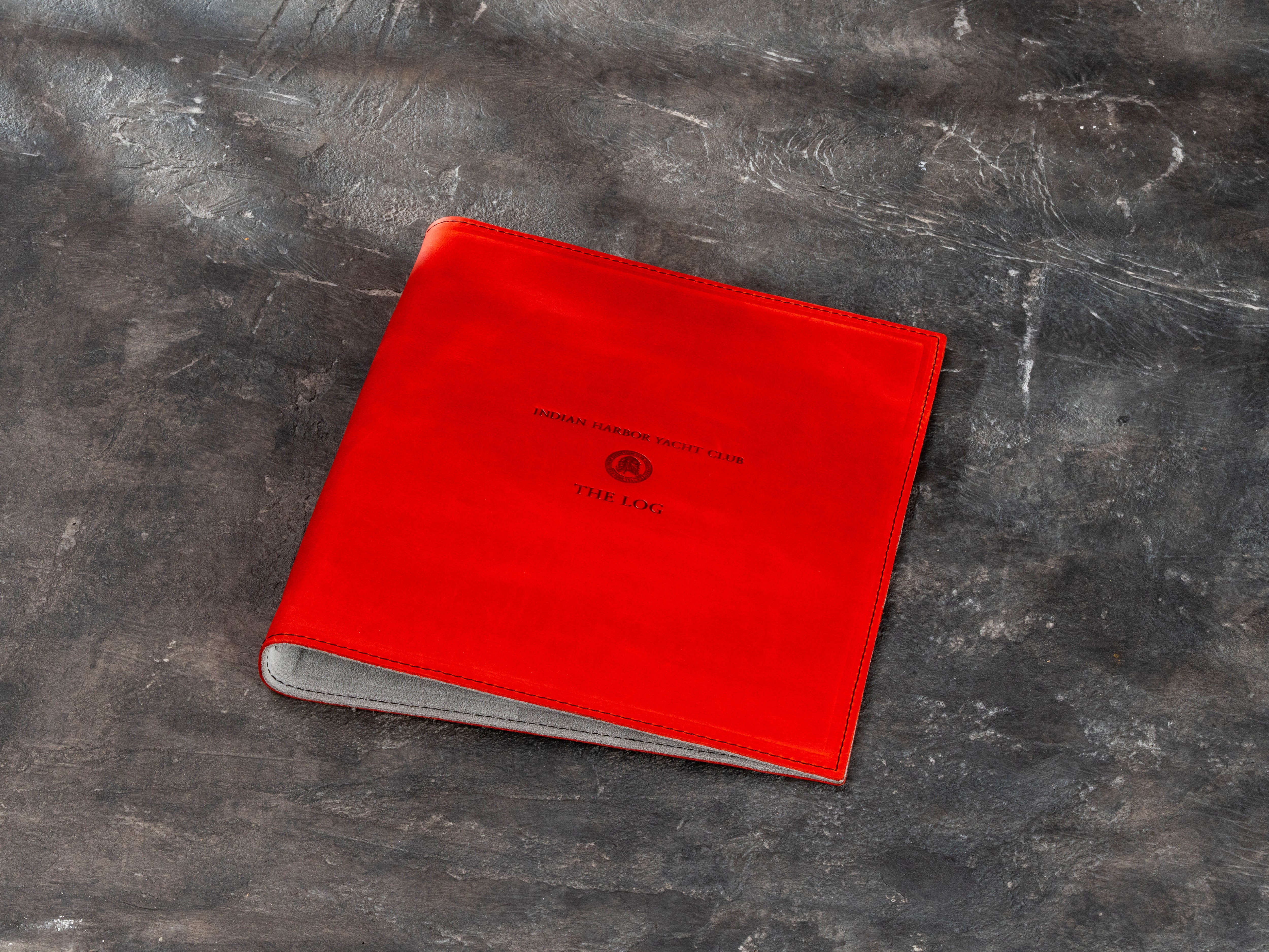 Bright red leather yacht club member logbook binder with custom club crest and The Log title on the front cover.