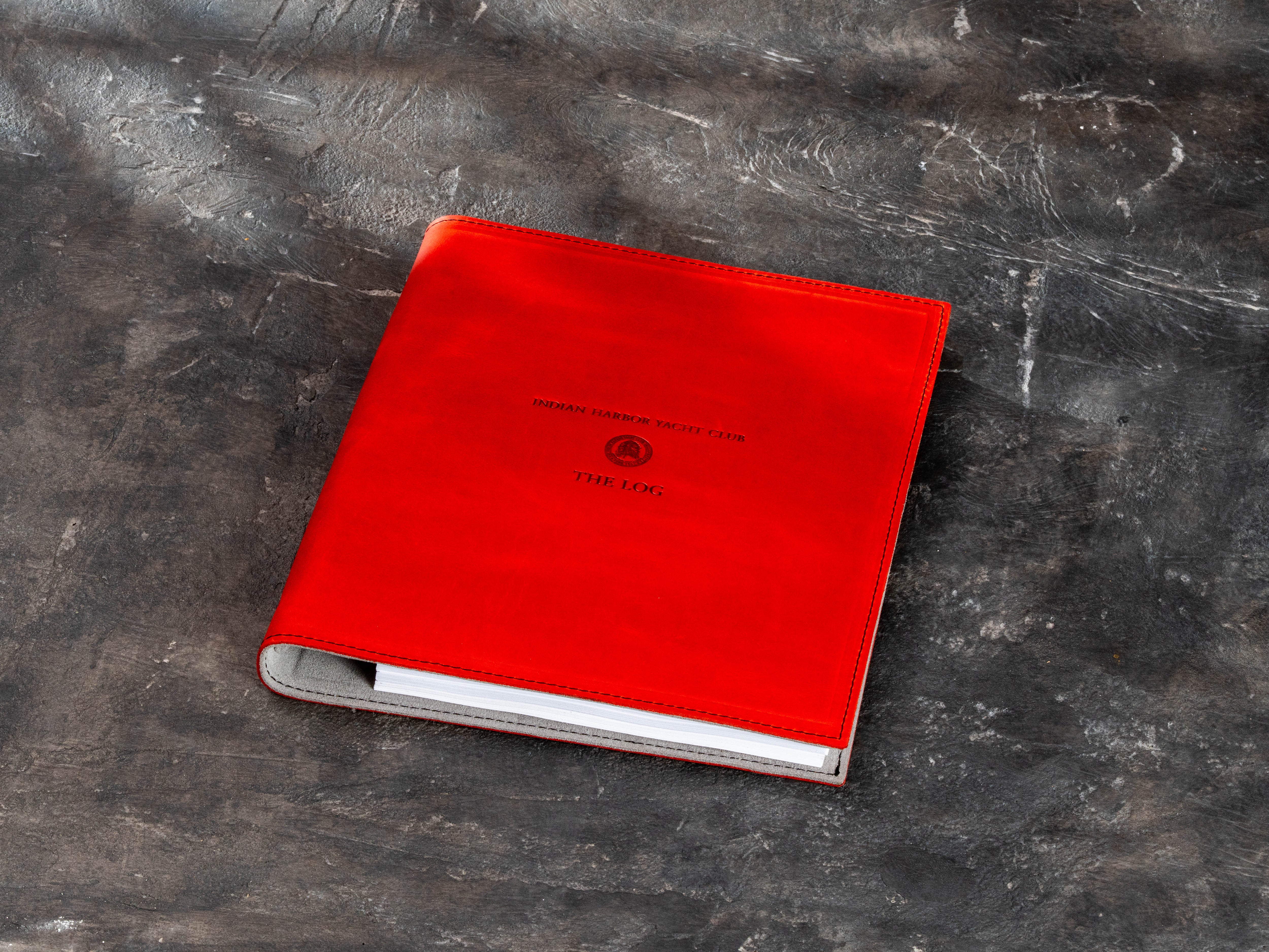 Red leather 3-ring sailing logbook binder with personalized yacht club emblem and printed pages visible inside.