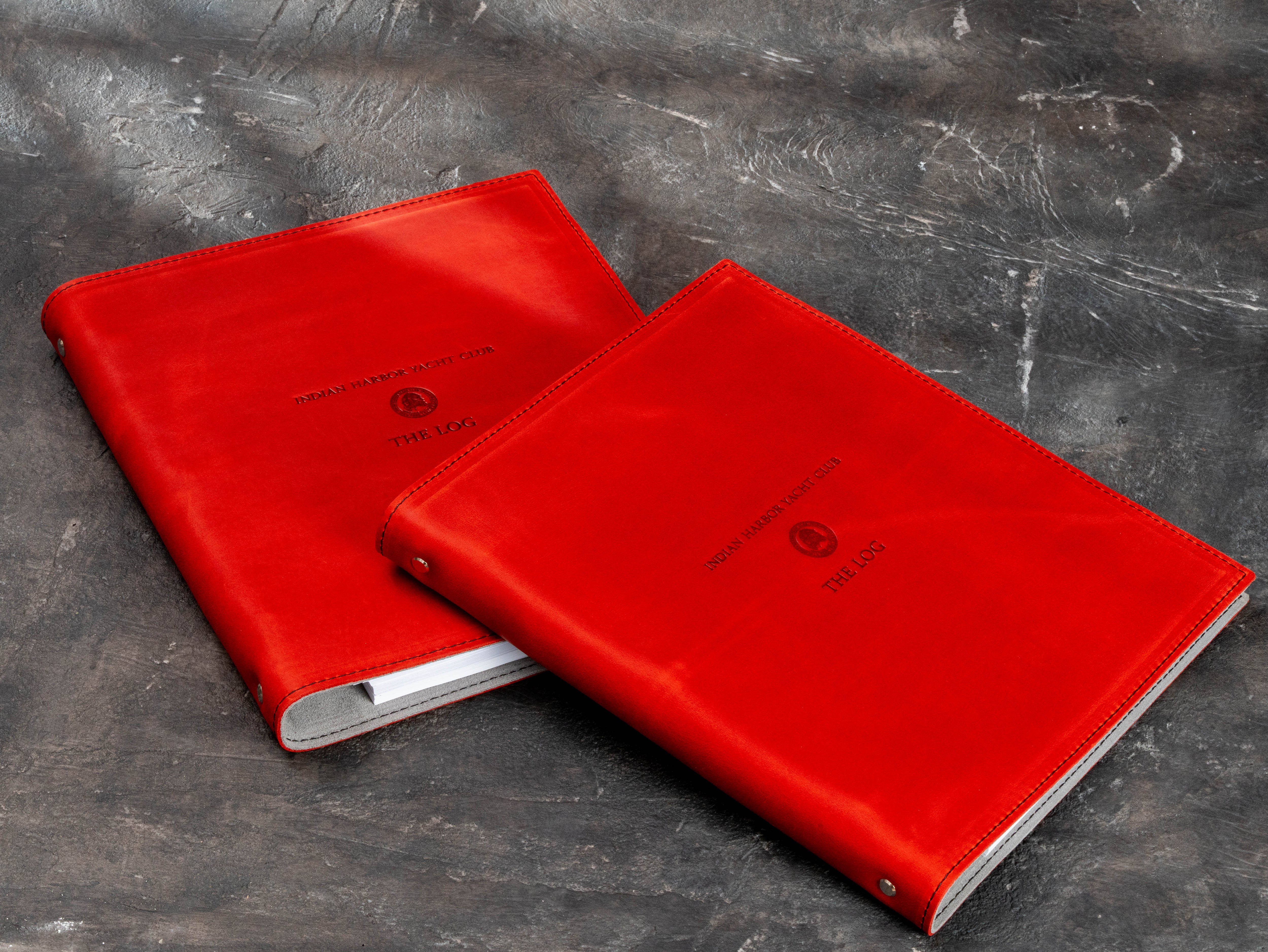 Two matching red leather yacht club logbook binders with custom crest, stitched covers and light interiors.