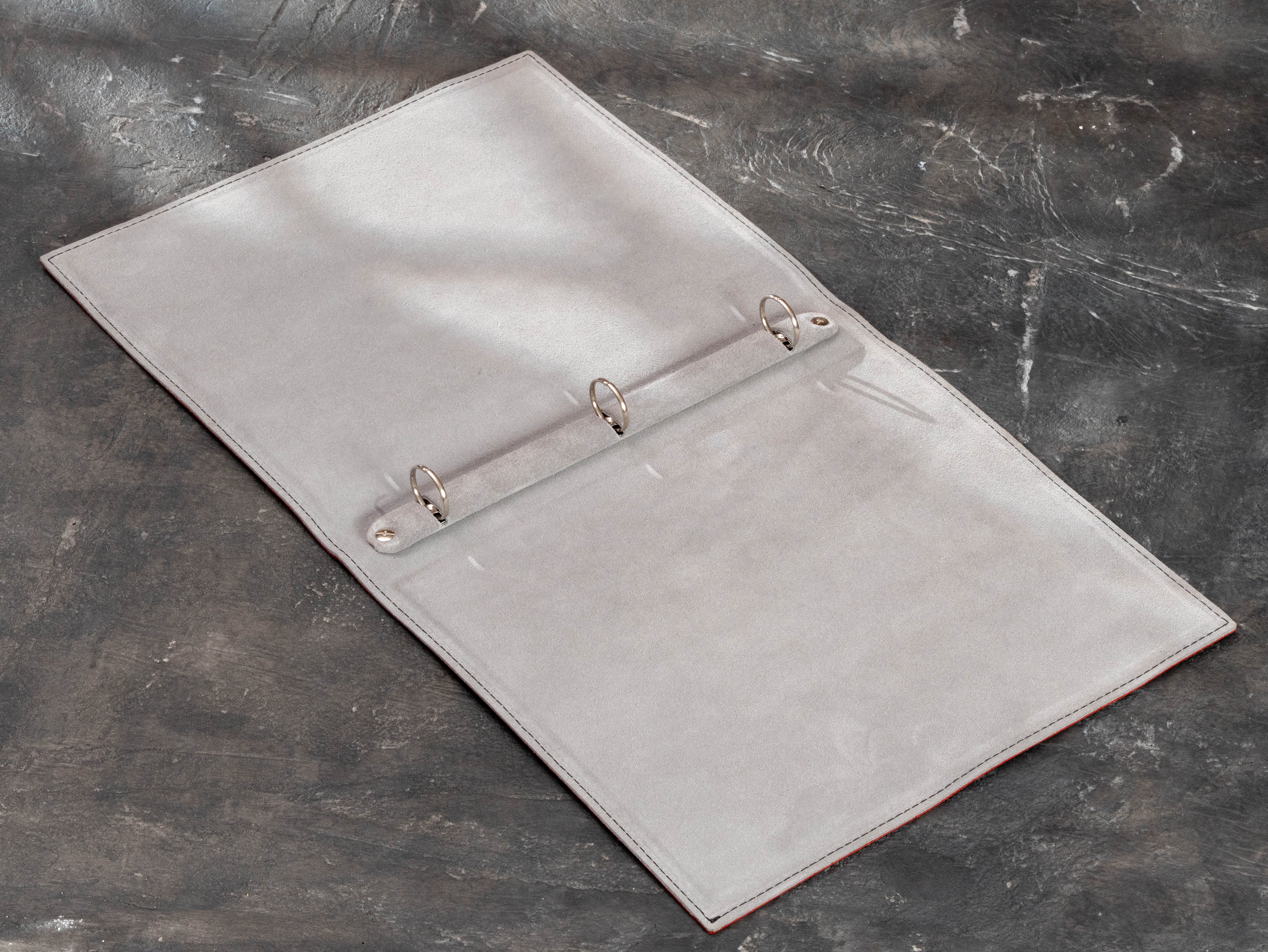 Interior view of red leather yacht club binder with light leather lining and three-ring mechanism for replaceable pages.
