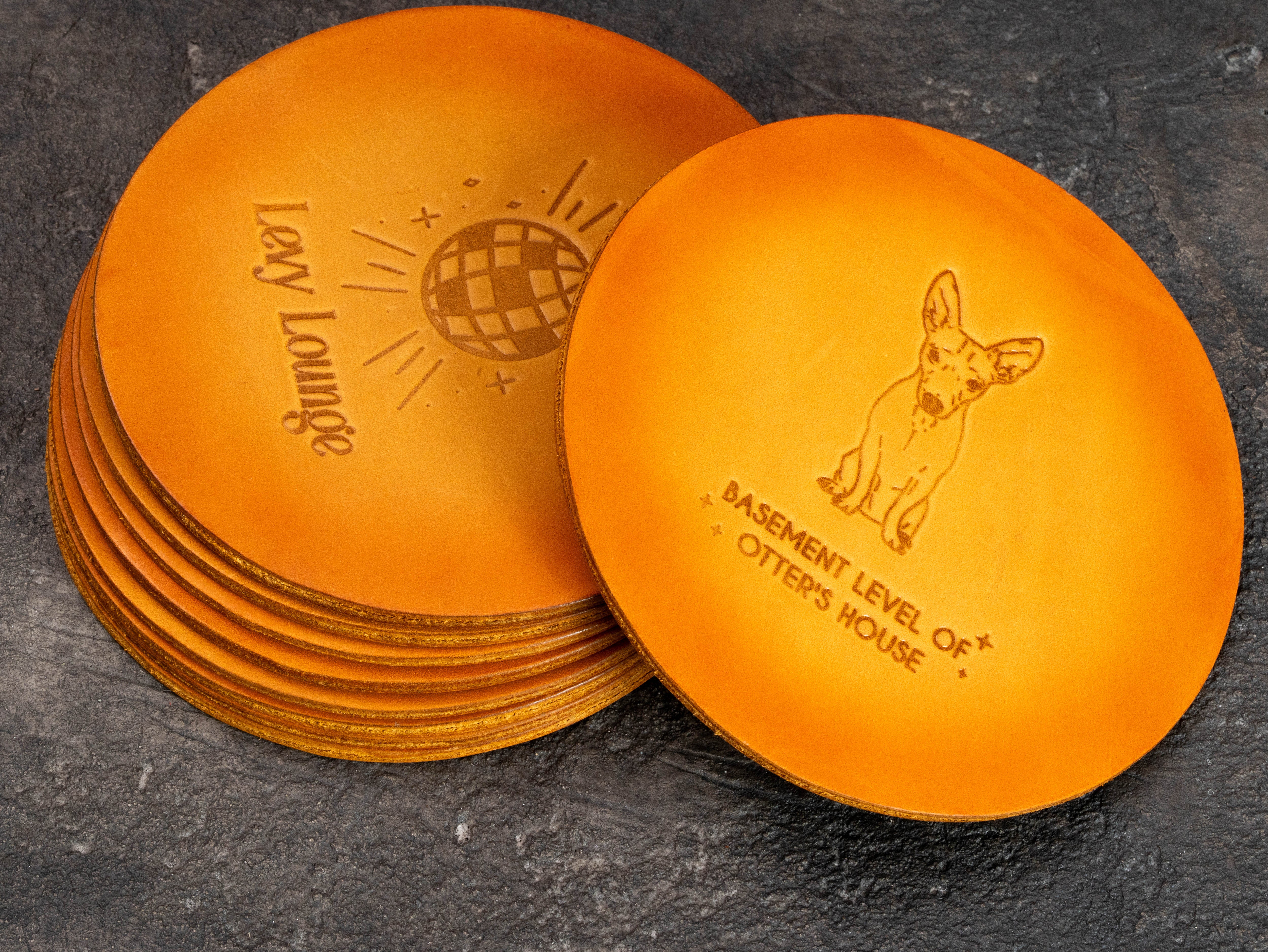 Double-sided personalized leather coaster showing two different custom embossed designs on a hand-colored round coaster