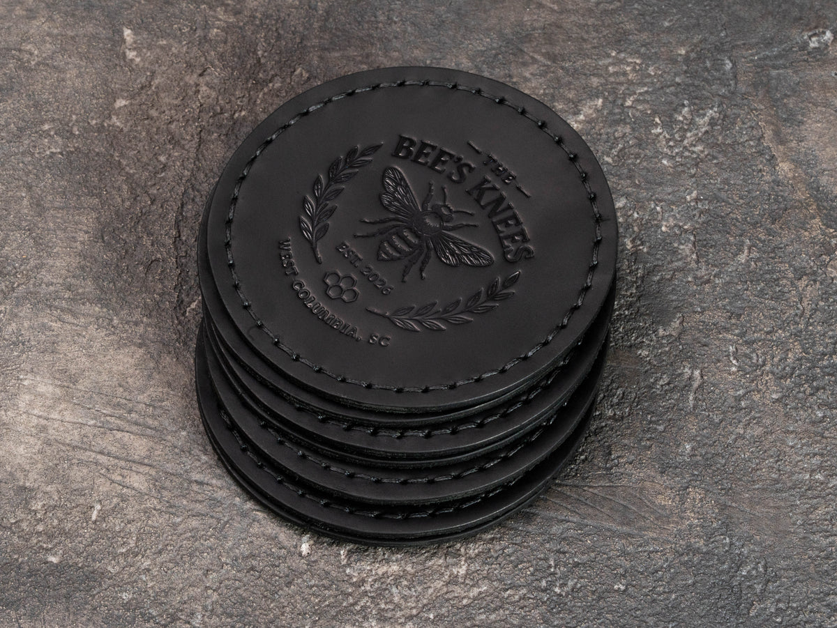 Black stitched leather club coasters with detailed bee logo, West Columbia South Carolina location and Est. 2026 embossing.