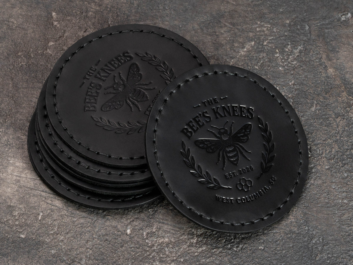 Custom black leather member gift coasters featuring a blind embossed bee crest, founding year and regional club identity.