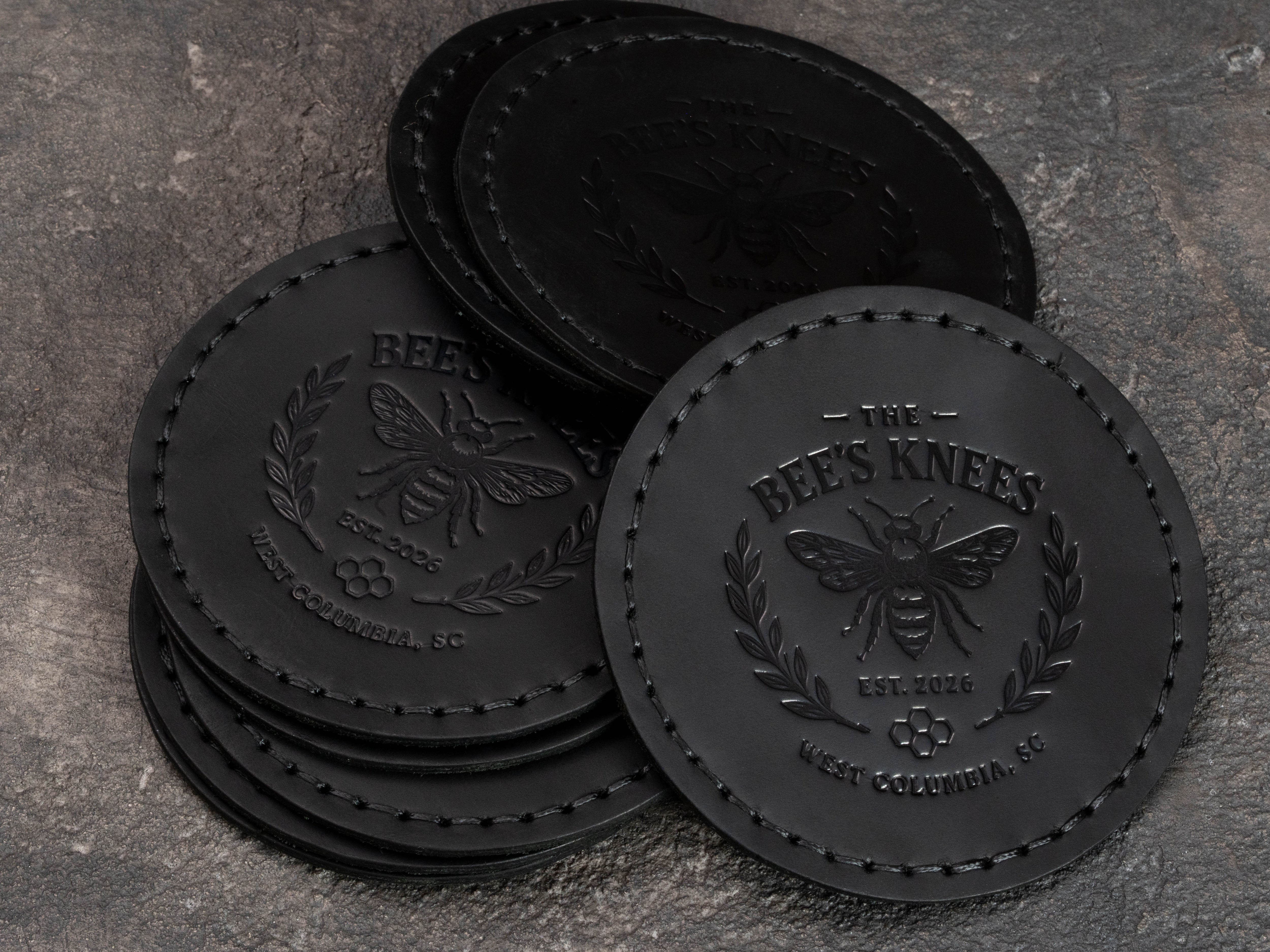 Set of black leather founding member coasters with tone-on-tone club logo embossing and stitched round edges.