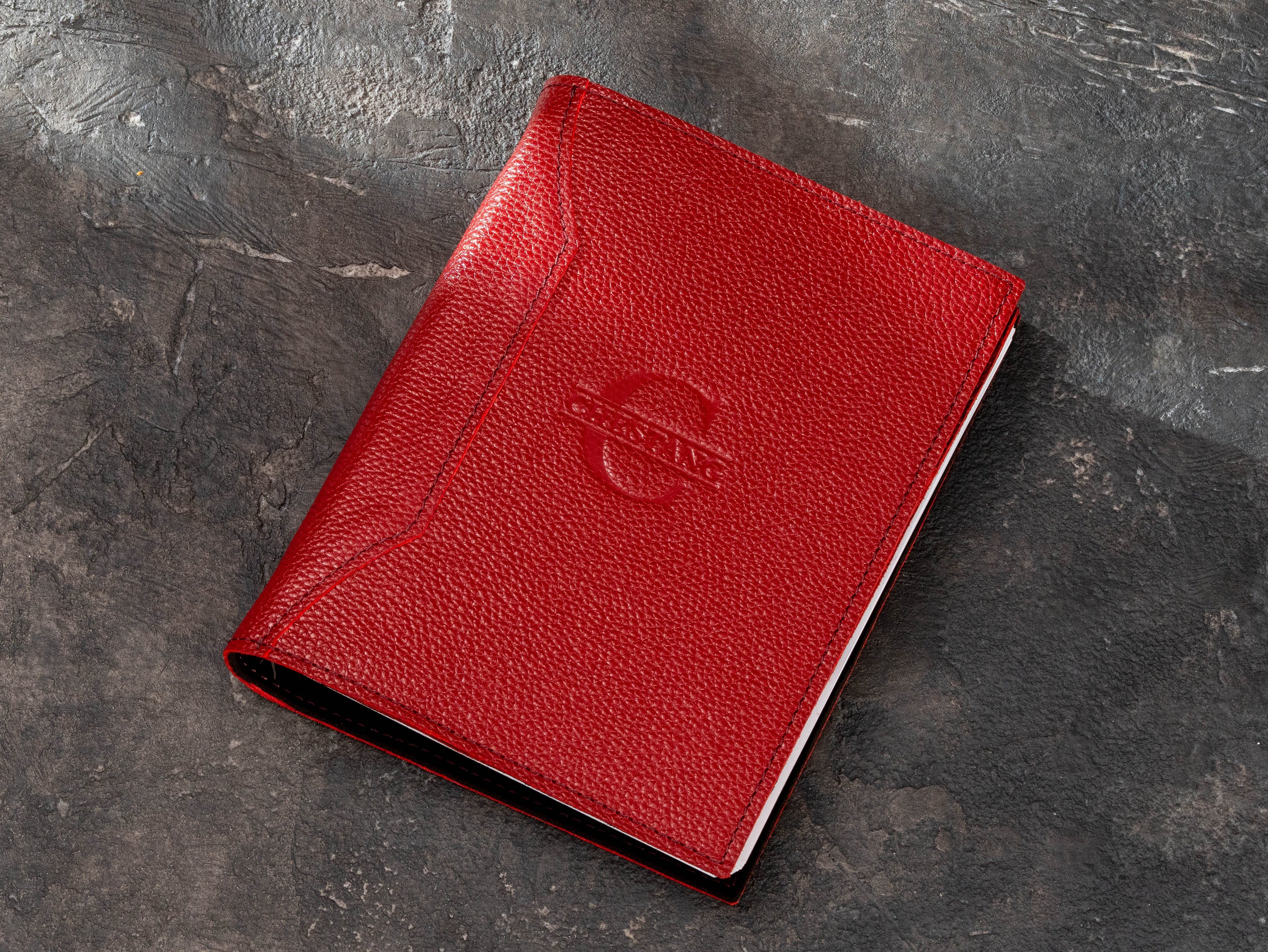 Closed red corporate leather ring binder organizer with tone-on-tone logo and white refill pages visible inside.