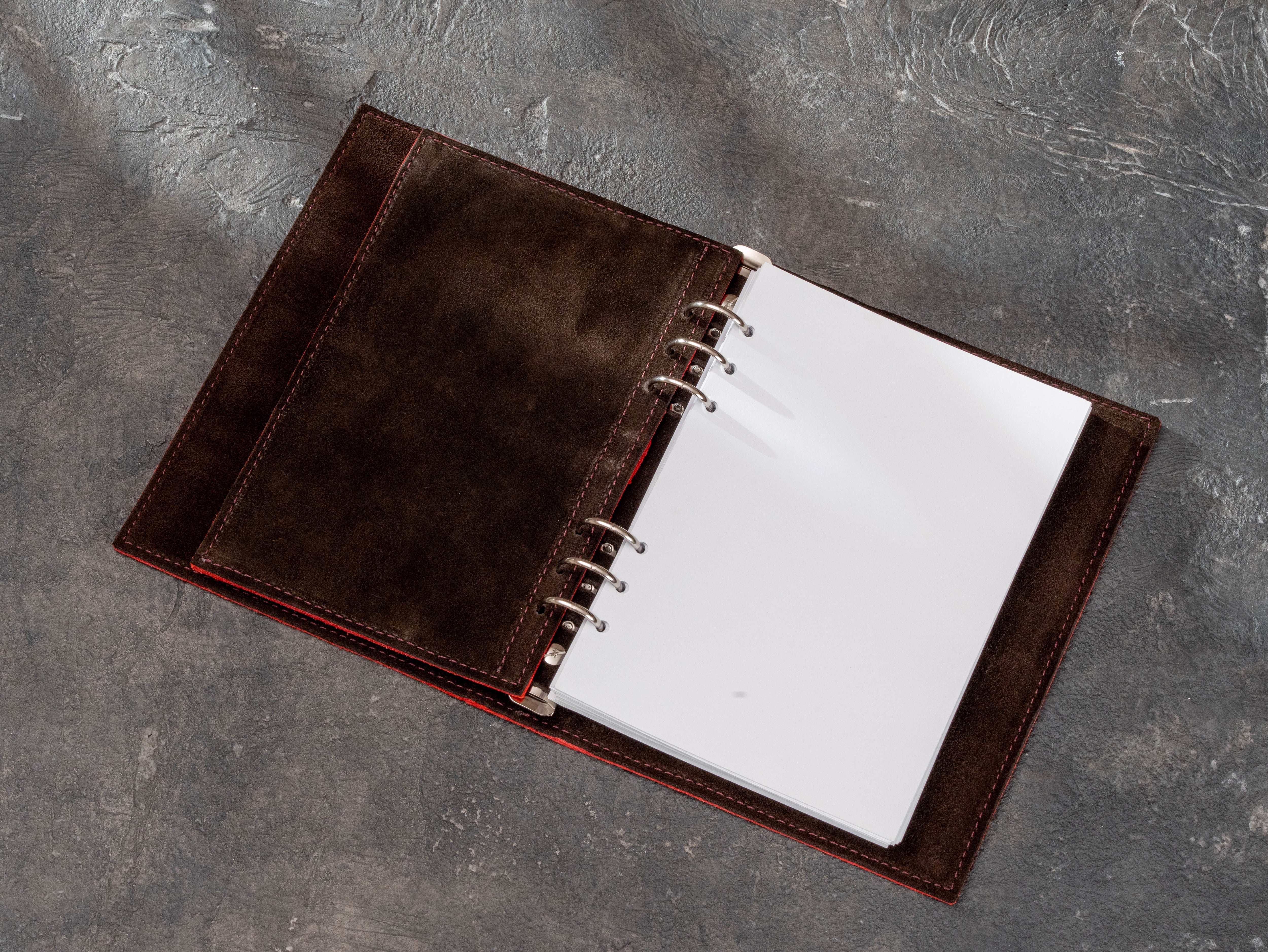 Corporate leather ring binder with removable organizer insert moved aside to show blank white refill pages and dark suede lining.