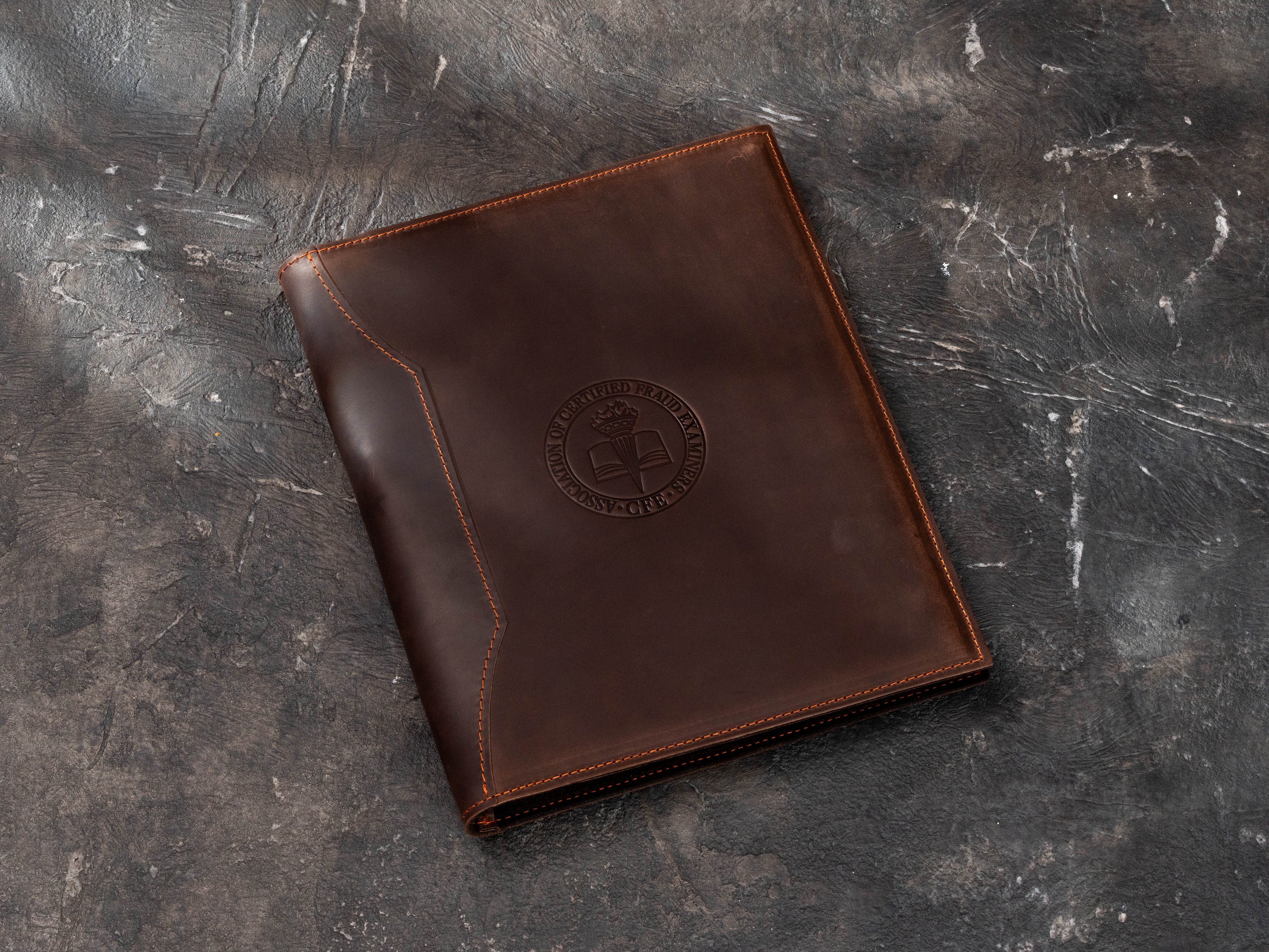 Dark brown leather professional association padfolio with custom embossed circular emblem and contrast stitching for corporate and membership gifts.