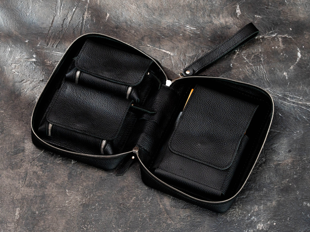 Black leather cigar organizer with open magnetic cigar compartment, removable oak tray and zippered accessory pockets.