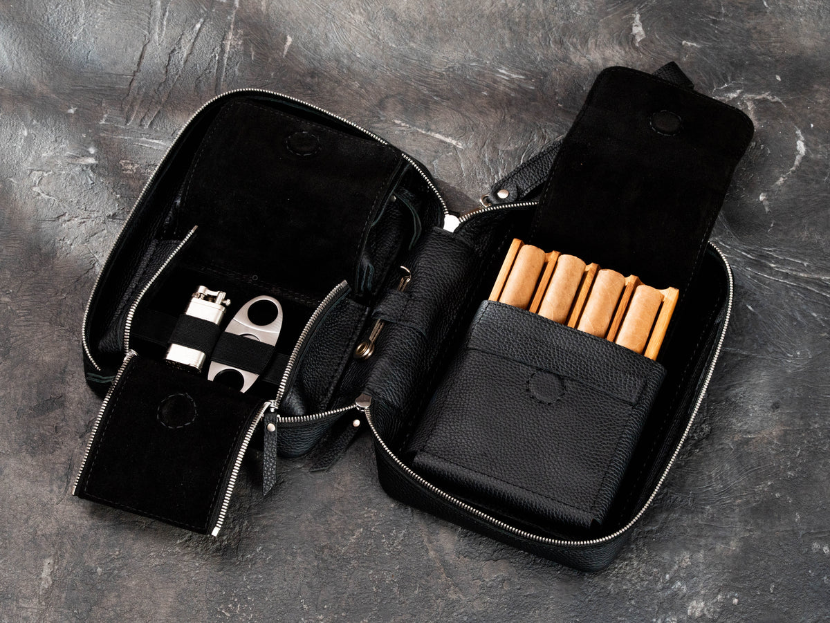 Open leather cigar club case showing oak cigar tray, accessory pocket with elastic holders, lighter and cigar cutter storage.