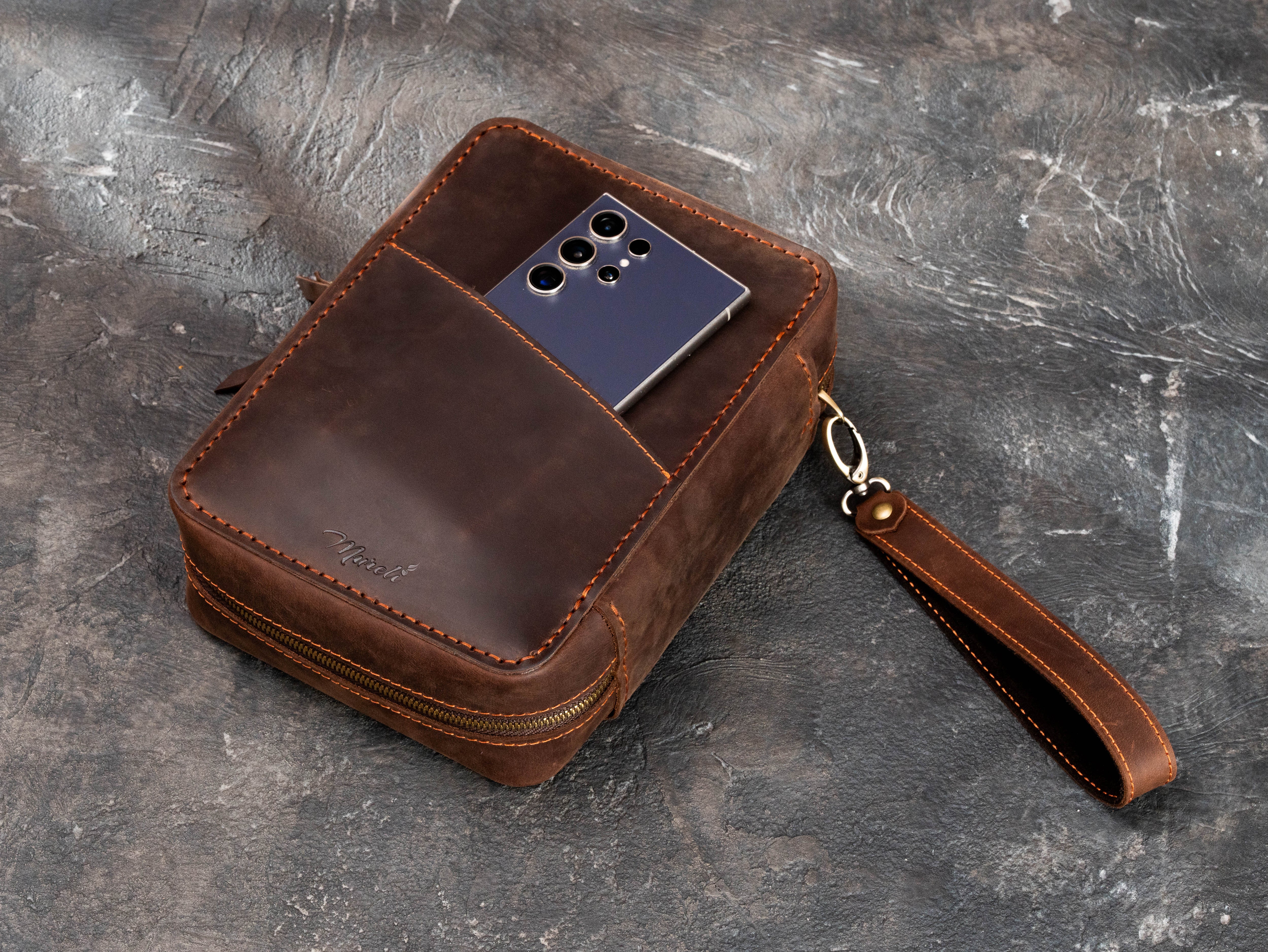 Brown leather cigar case with exterior phone pocket, removable wrist strap and dual zipper closure for club and event use.