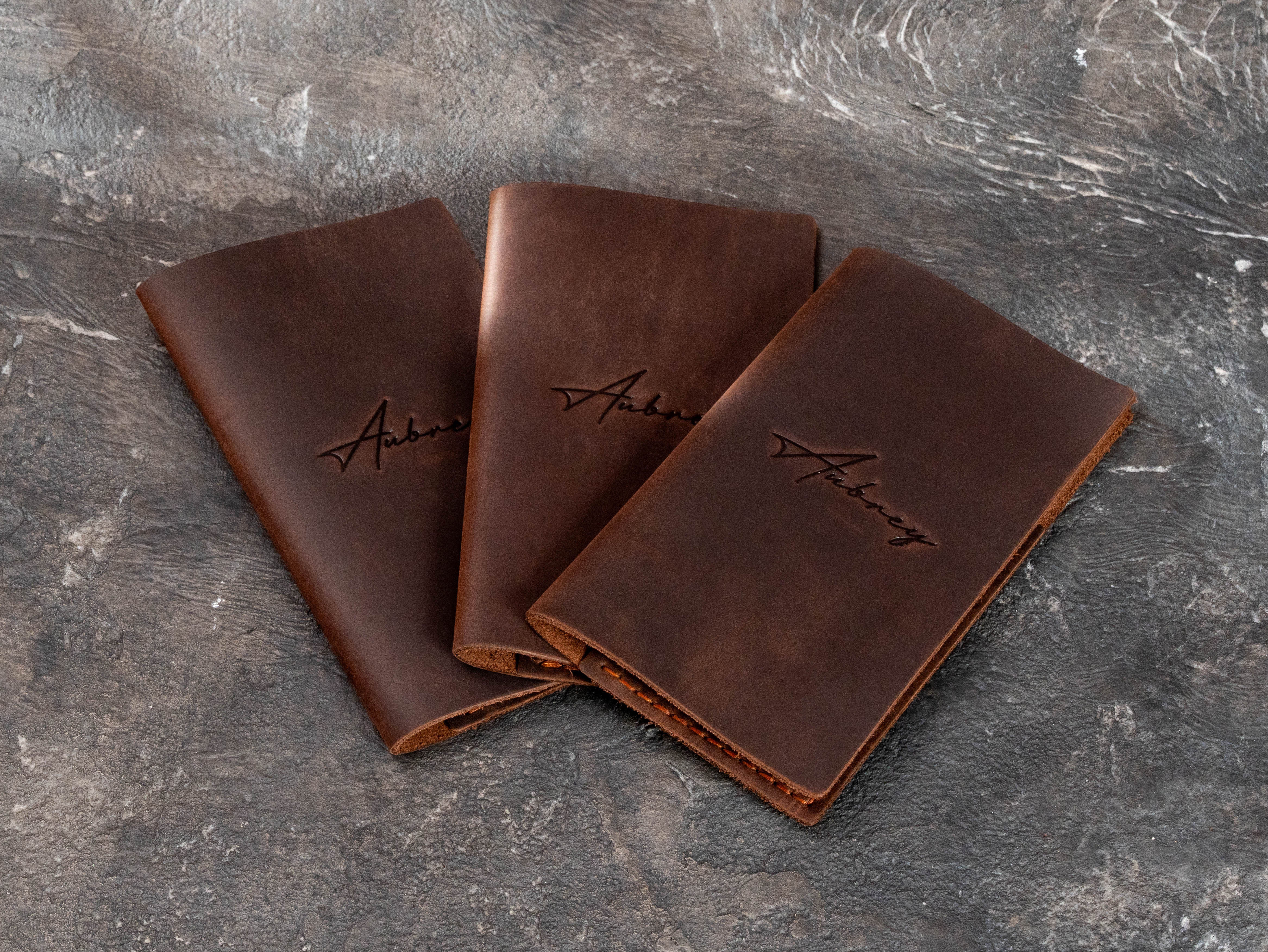 Three brown leather restaurant check presenters with custom Aubrey logo and slim Design No. 1 construction.