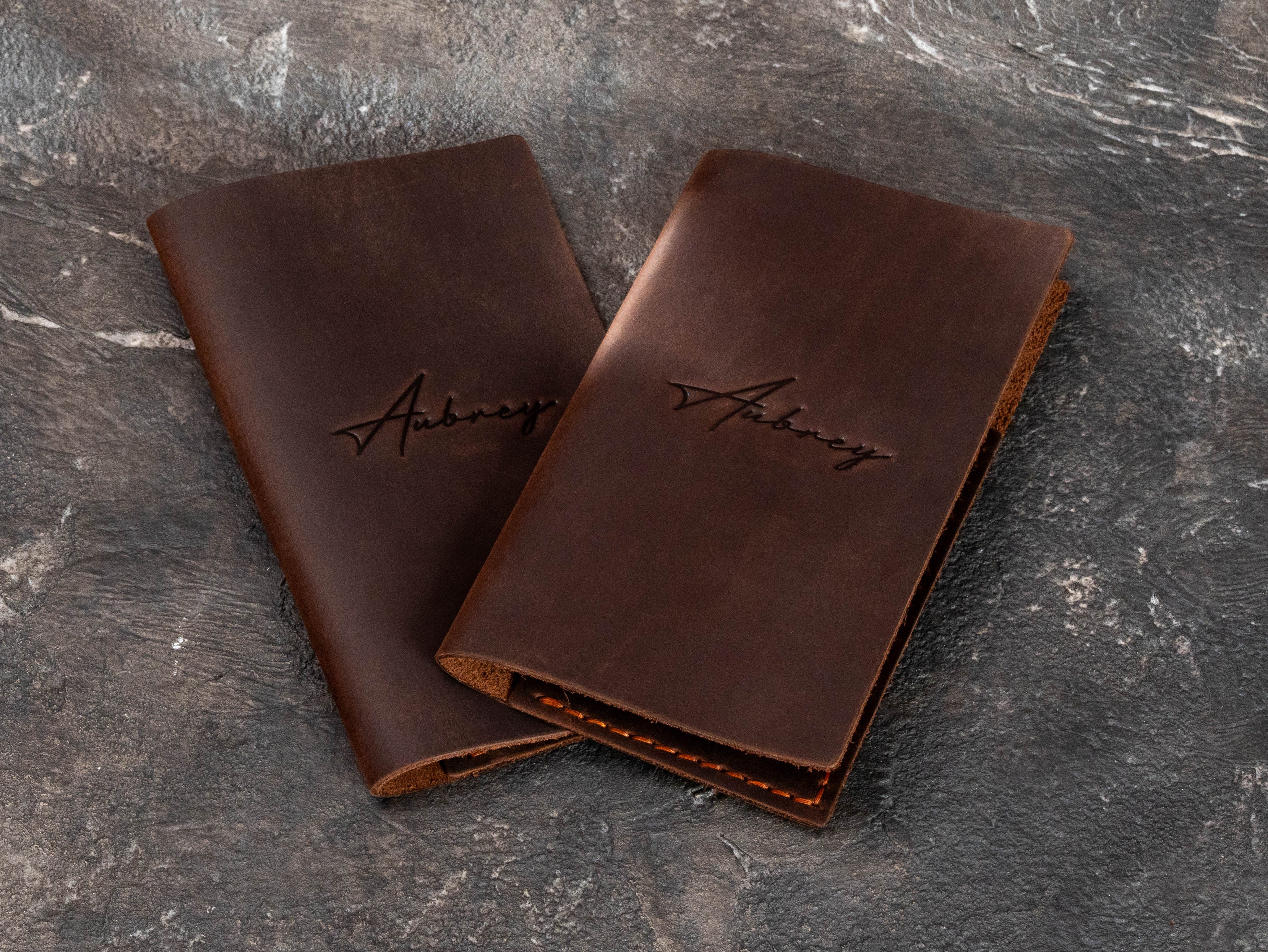 Two personalized brown leather guest check holders with blind embossed restaurant logo for fine dining service.