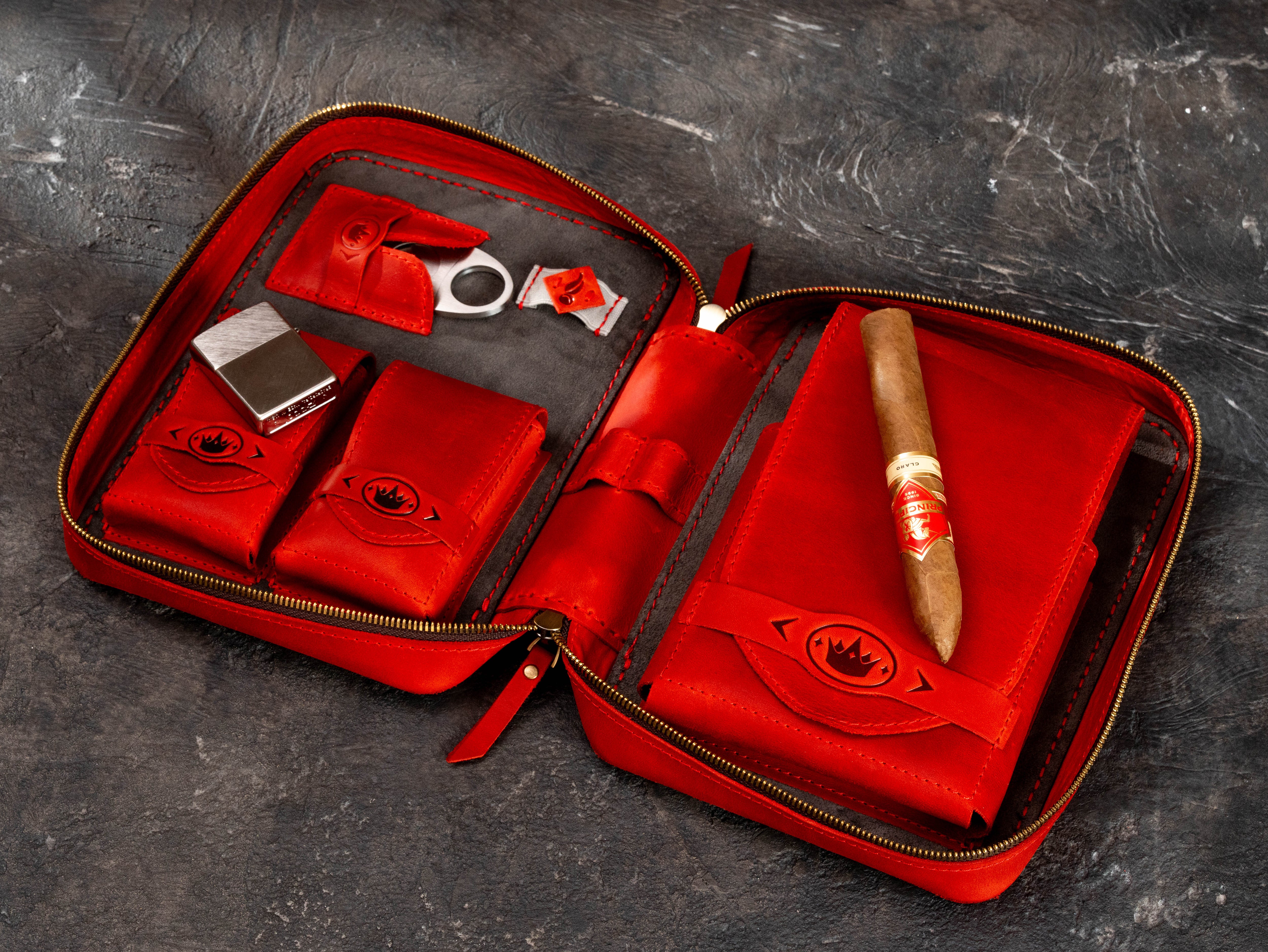 Red leather cigar organizer displayed with cigar, lighter and cutter in dedicated interior accessory compartments.