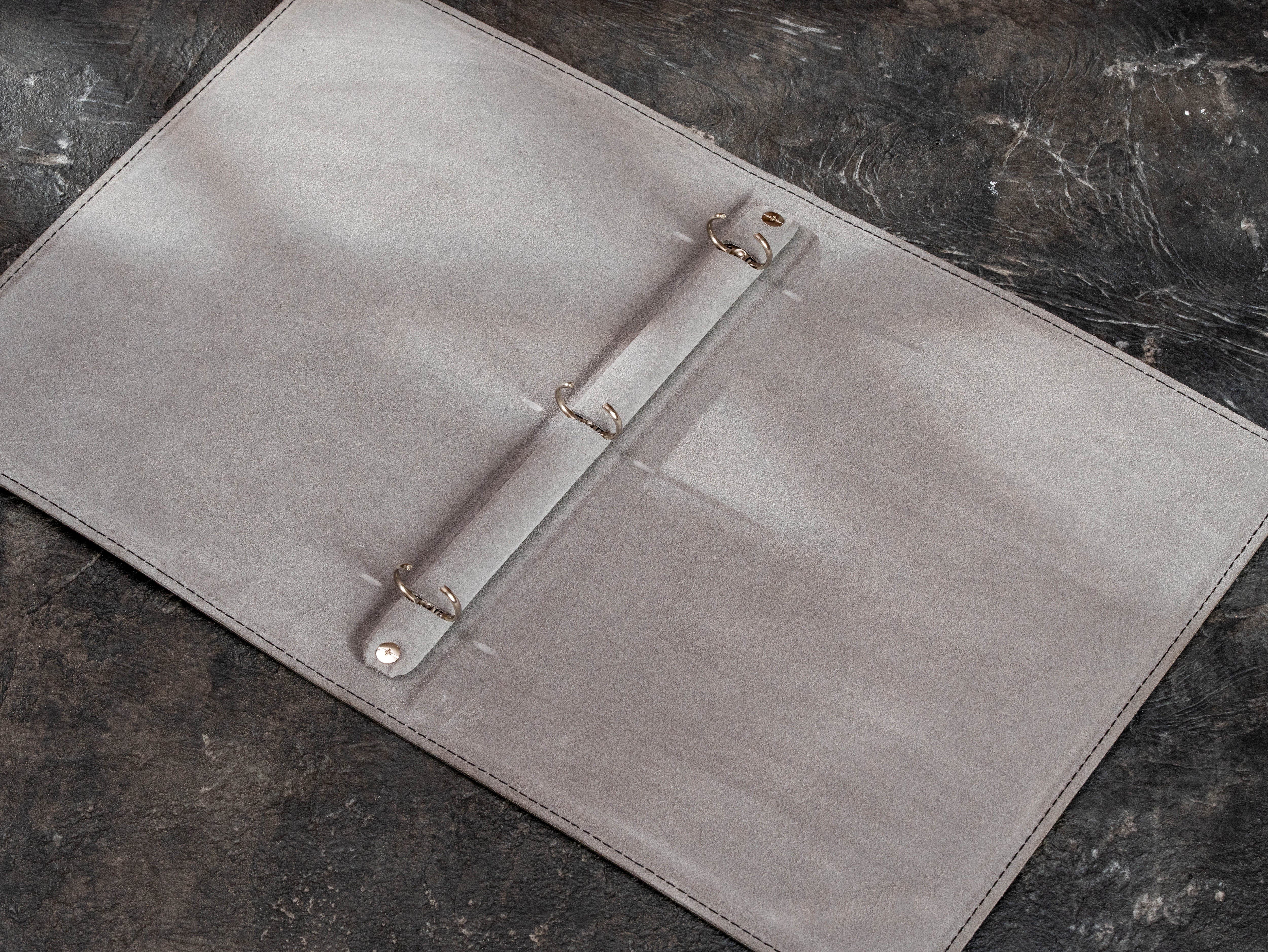 Open custom corporate leather binder showing three-ring mechanism and minimalist light gray suede lining.