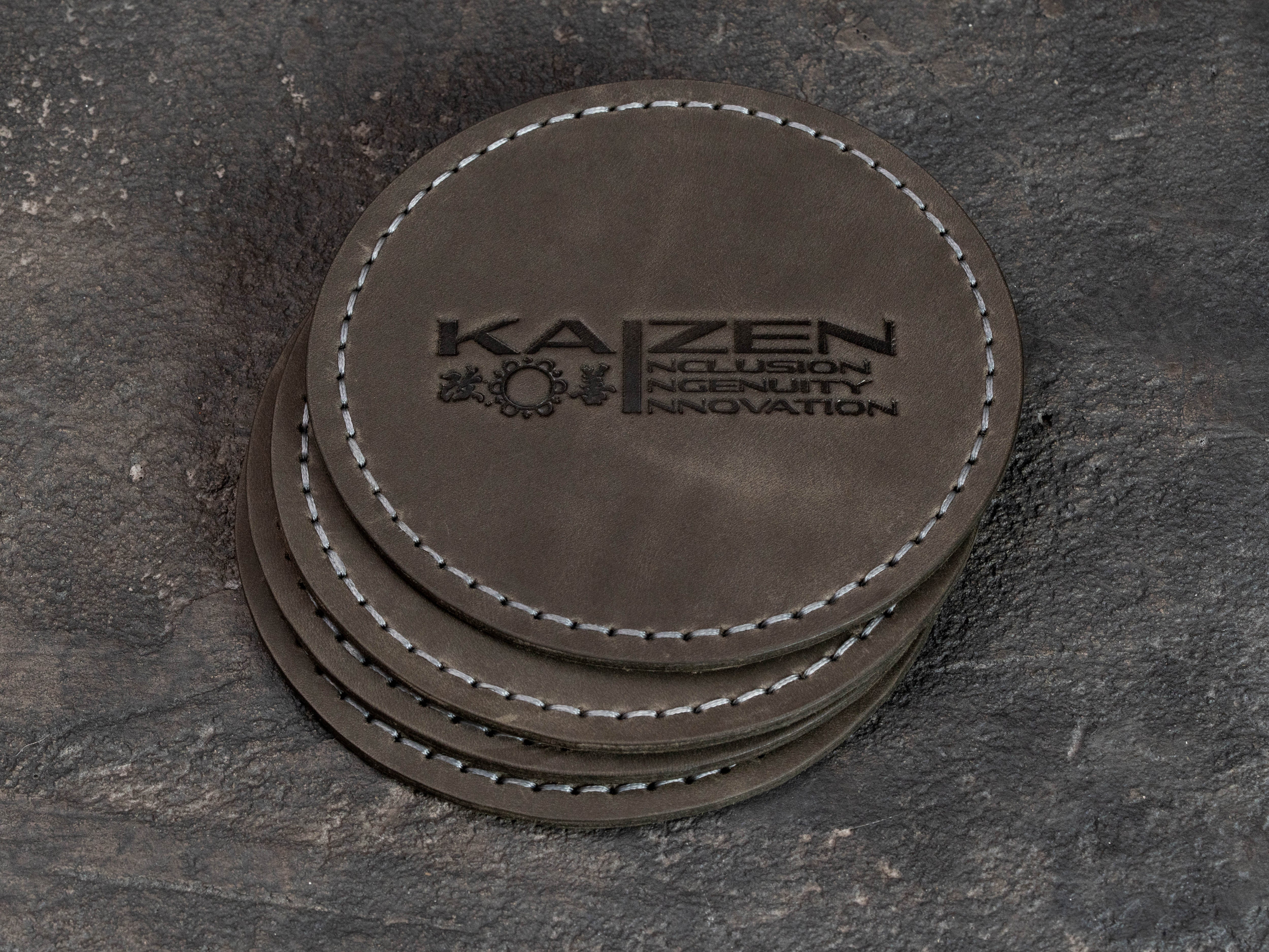 Hand-stitched Gray leather coasters with custom company logo displayed on matching machine-stitched equipment mat.