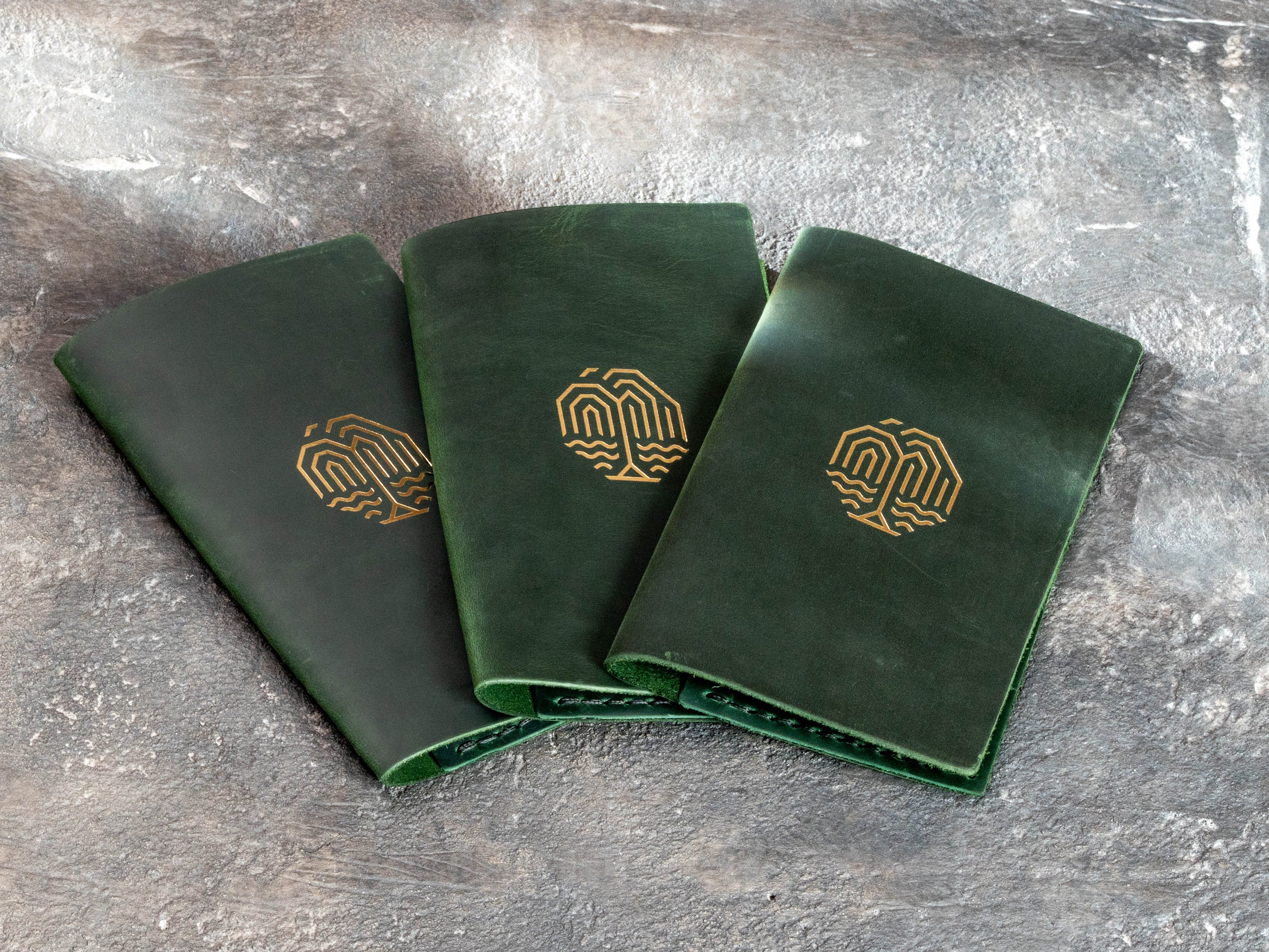 Green leather restaurant bill holders showing the front logo personalization and stitched edges.