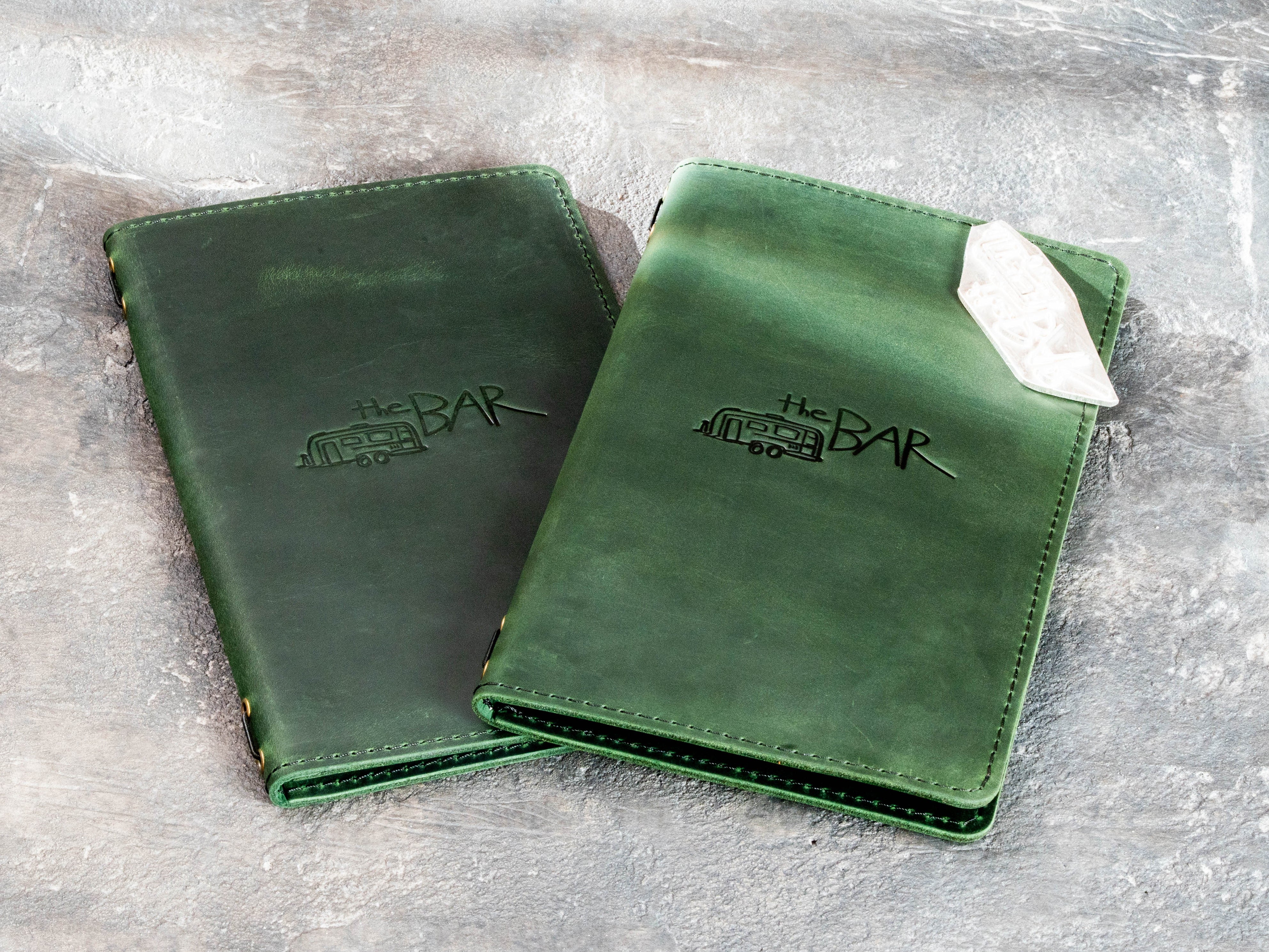 Green leather menu covers with custom bar logo embossing and stitched double-layer construction.