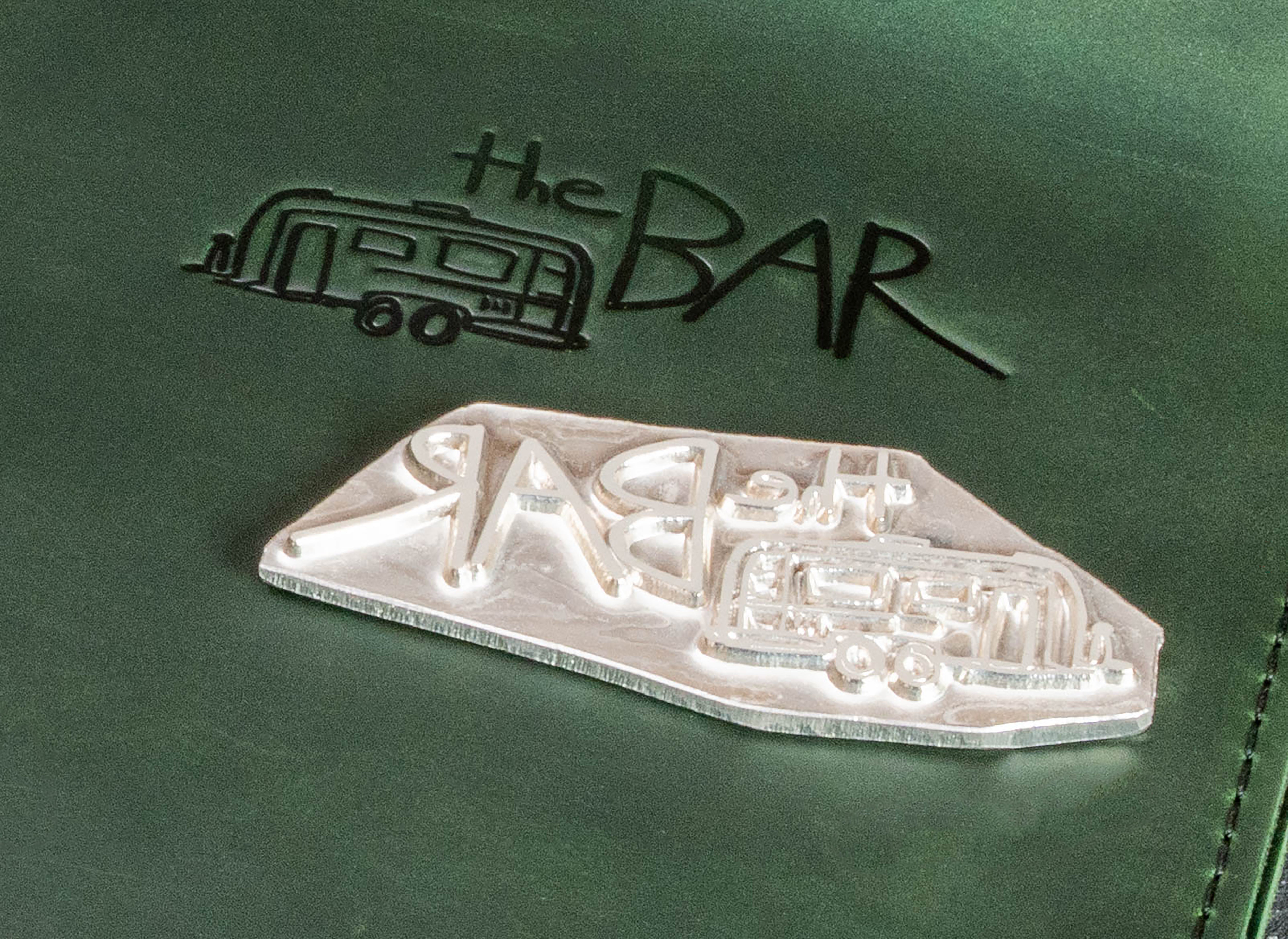 Close-up of custom metal embossing die next to the finished logo impression on green leather.